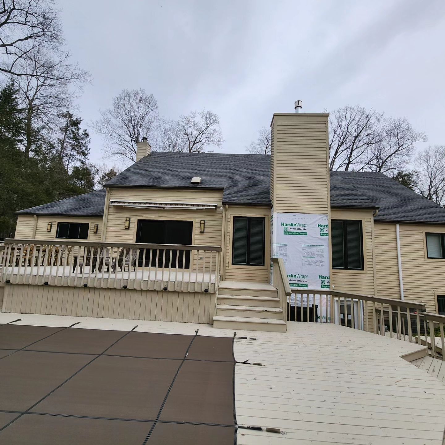 Beige house with a deck and covered pool. Black windows, and a chimney. Overcast sky.