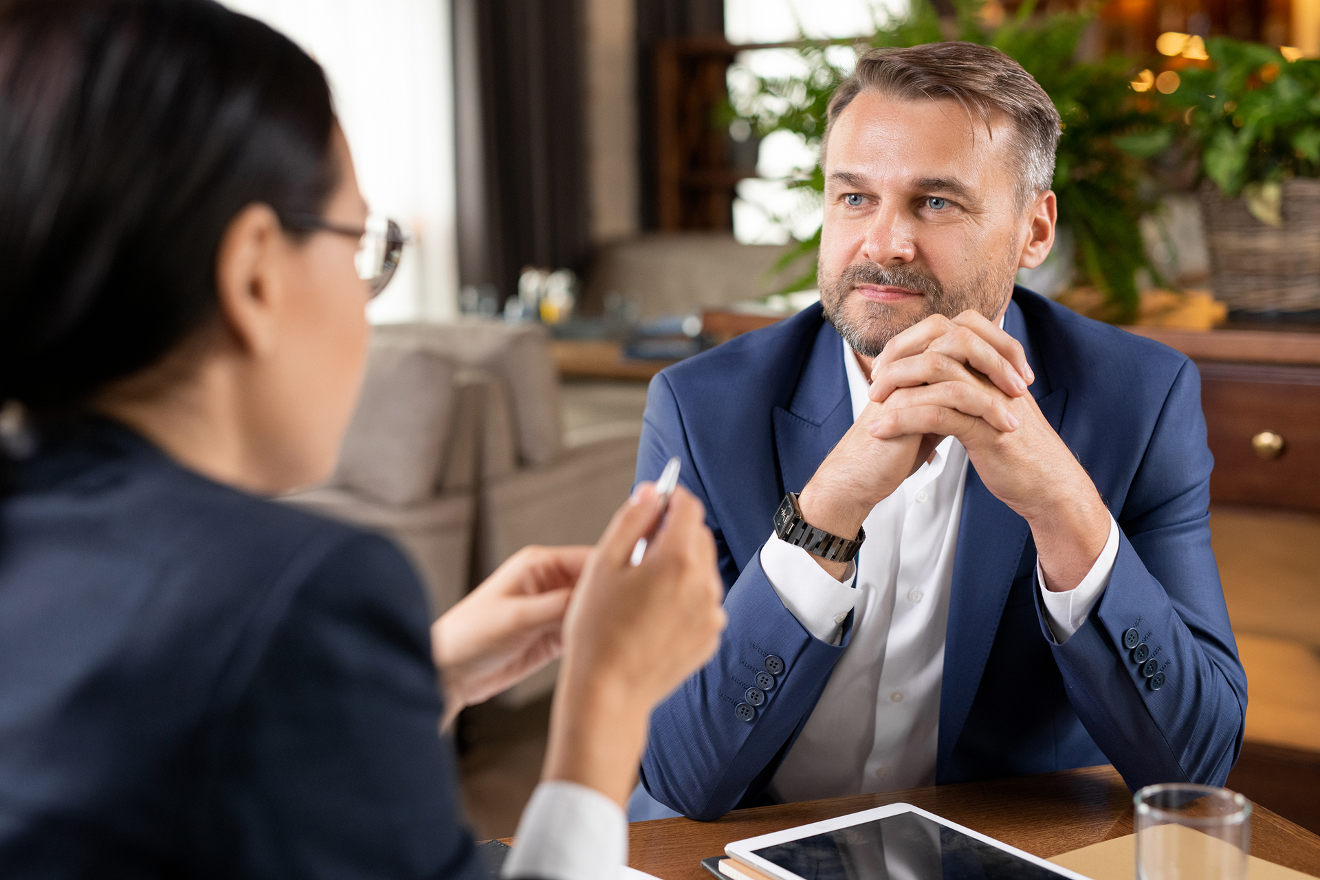Two people in business attire talking across a table in a warm office setting.