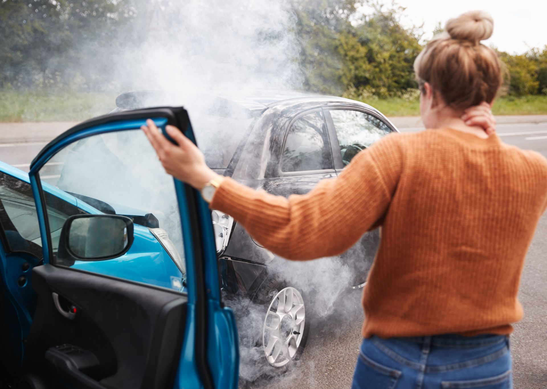 Woman beside blue car with shattered windshield after a crash, holding the open door in rain