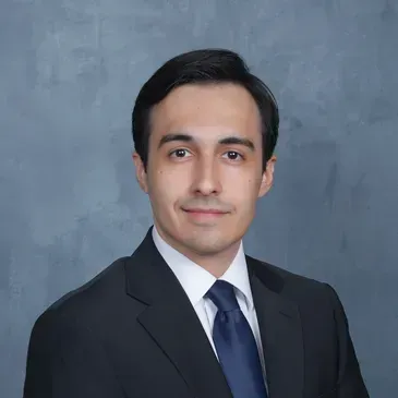 Studio headshot of a man in a dark suit and tie against a gray backdrop