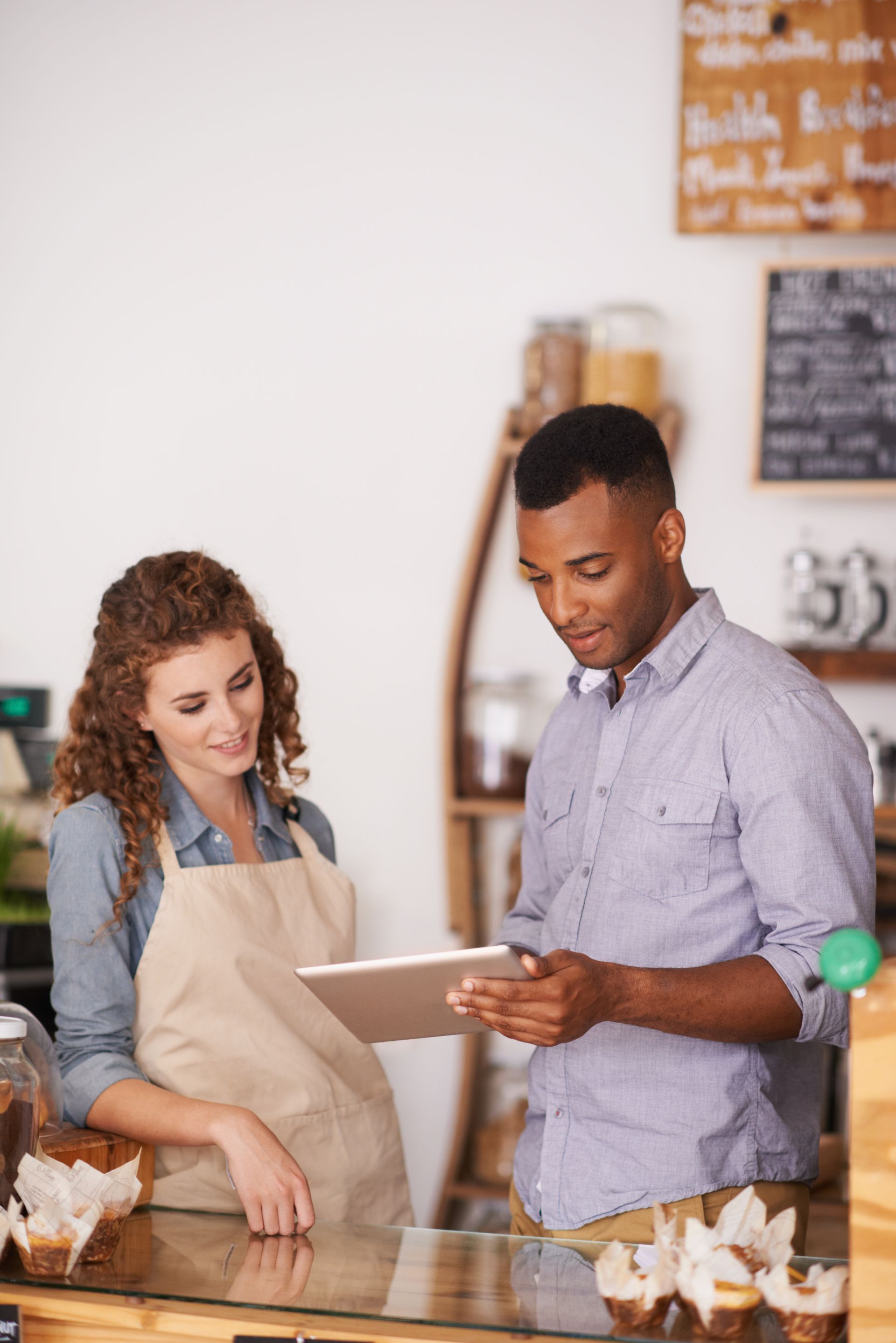Two people in aprons review notes at a bakery counter, with pastries displayed in front.