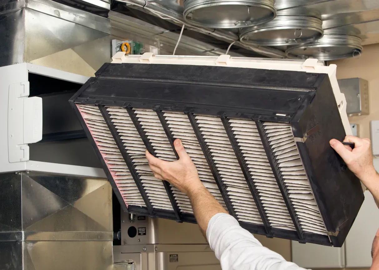 Hands removing a dirty HVAC air filter from a metal ventilation system