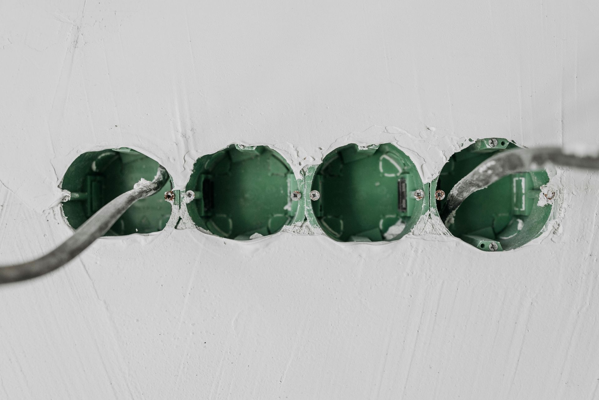 Four green electrical junction boxes in a wall, with exposed wires and unfinished drywall.