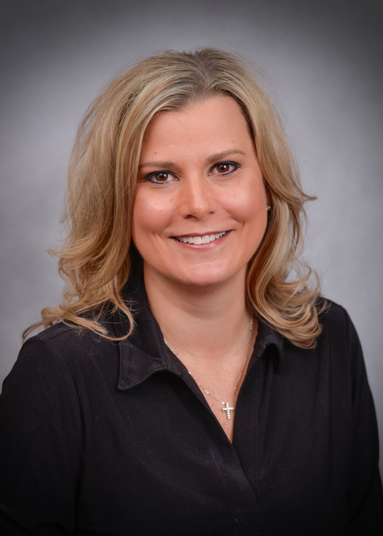 A woman wearing a black shirt and a cross necklace is smiling for the camera.