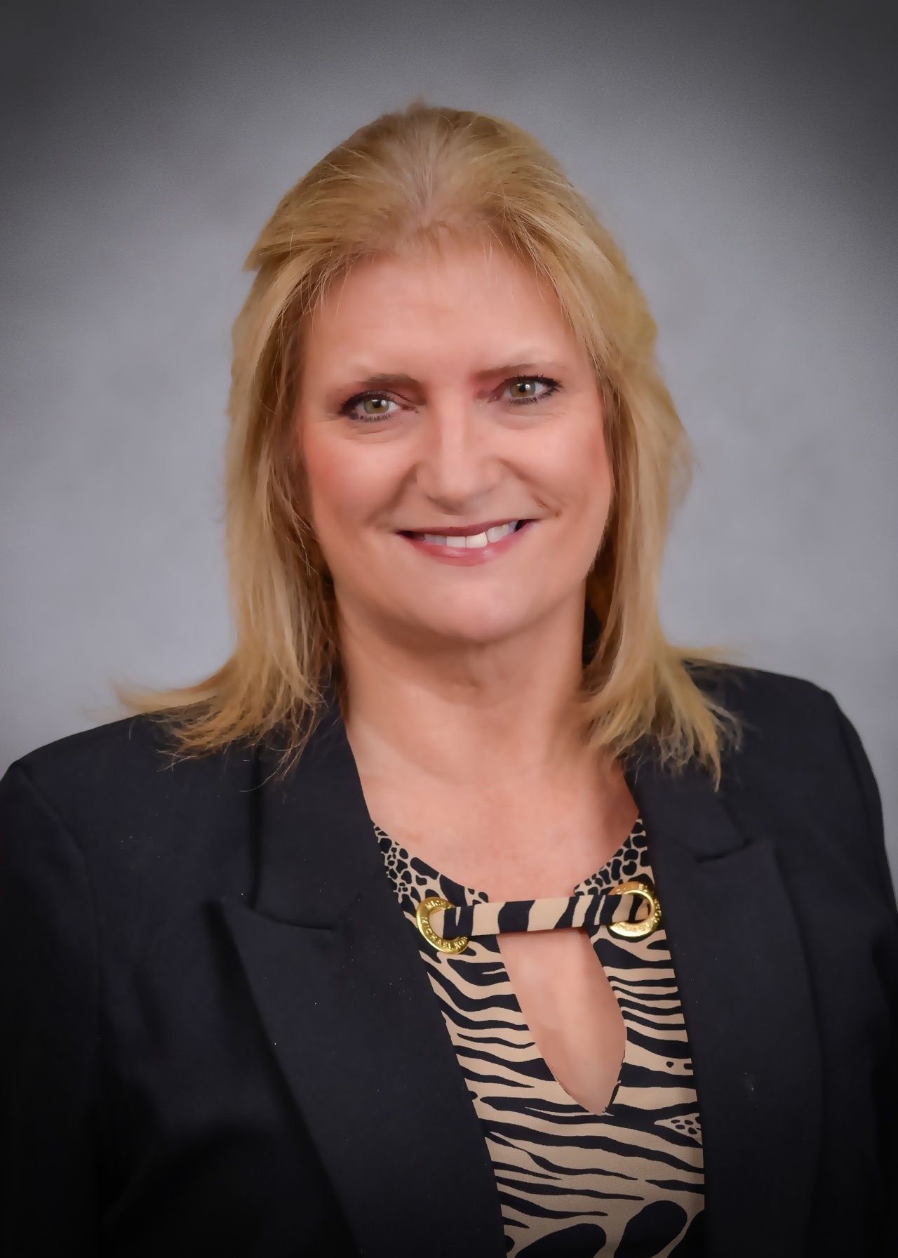 A woman wearing a black jacket and a zebra print shirt is smiling for the camera.