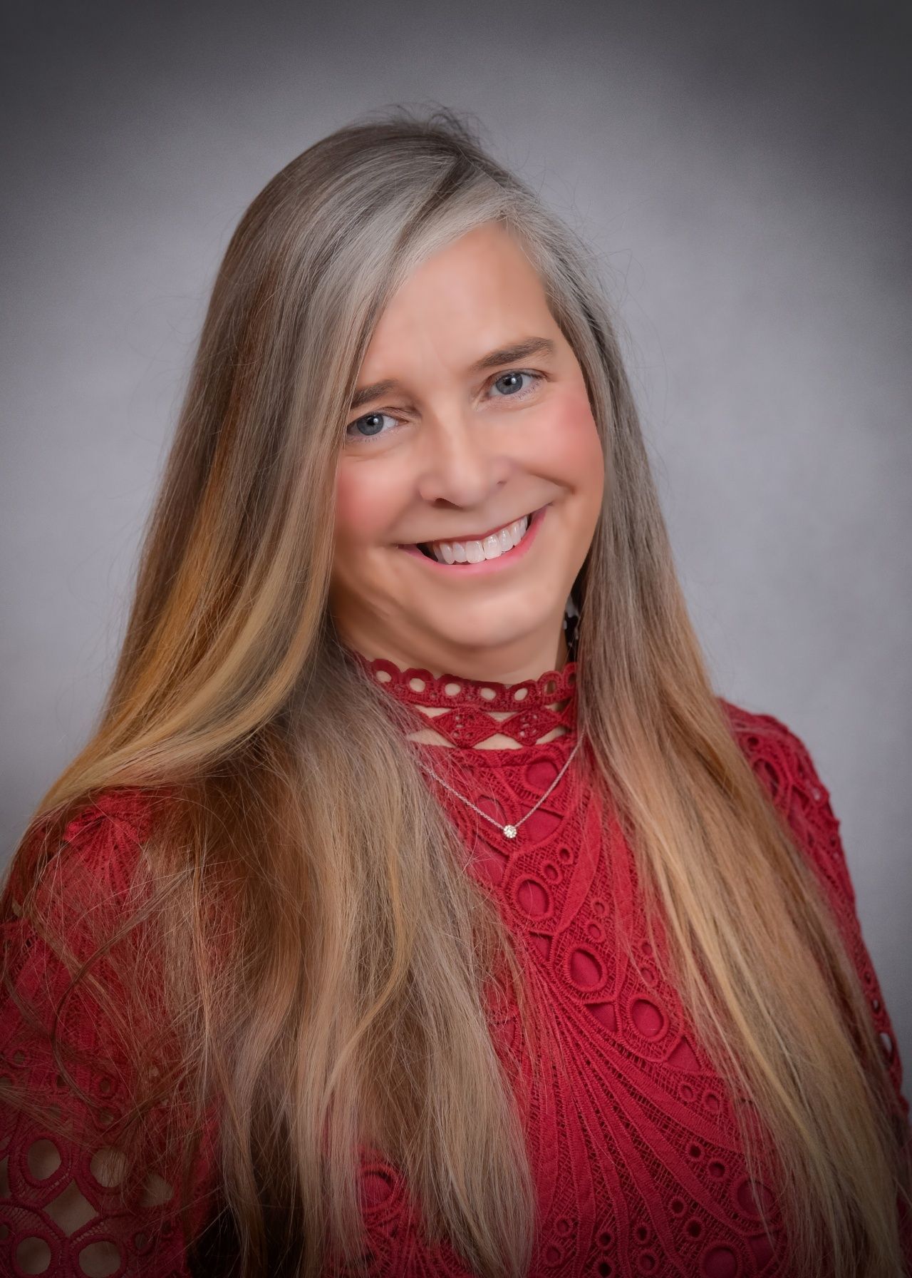 A woman with long hair is wearing a red sweater and smiling for the camera.
