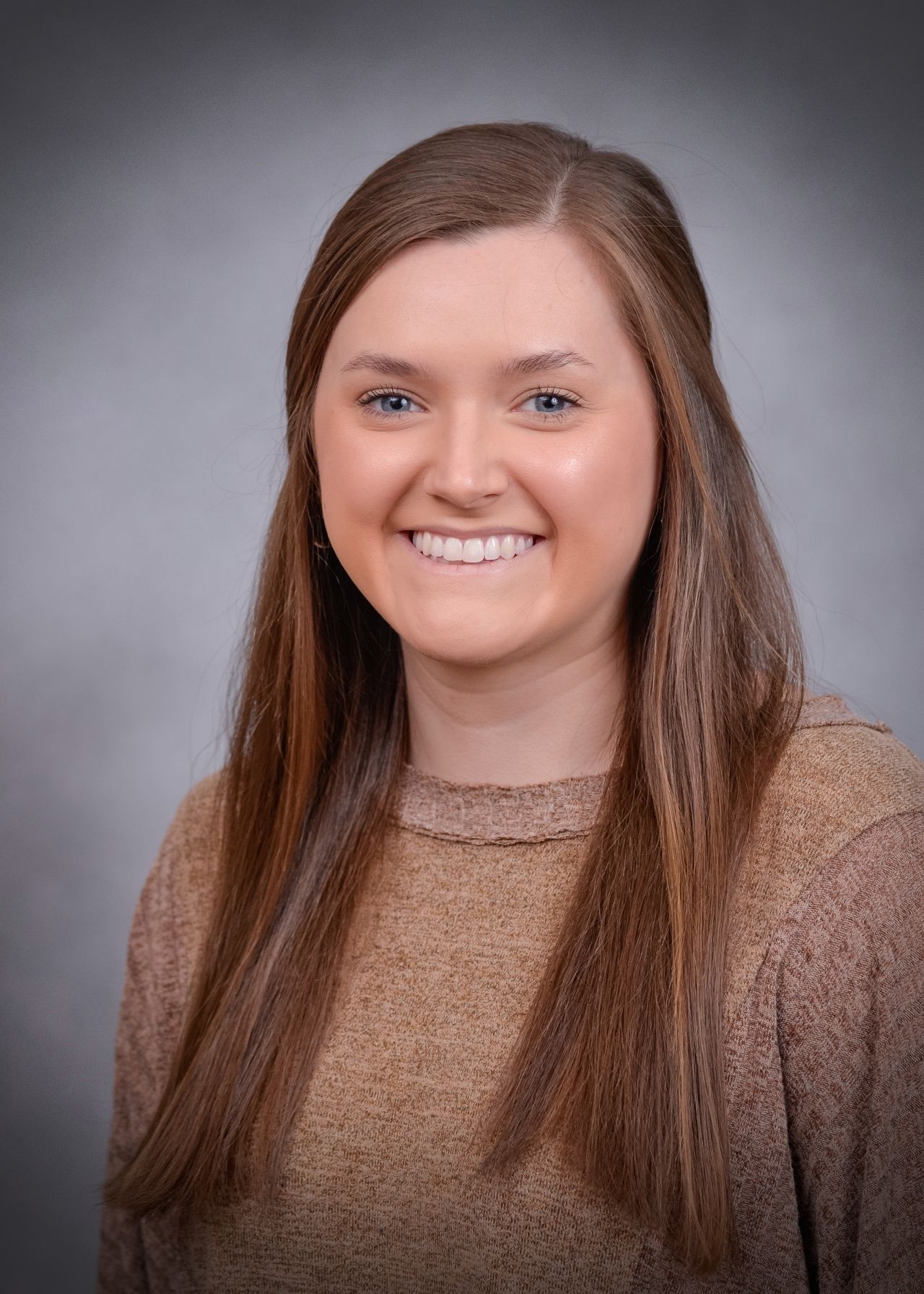 A woman in a brown sweater is smiling for the camera.