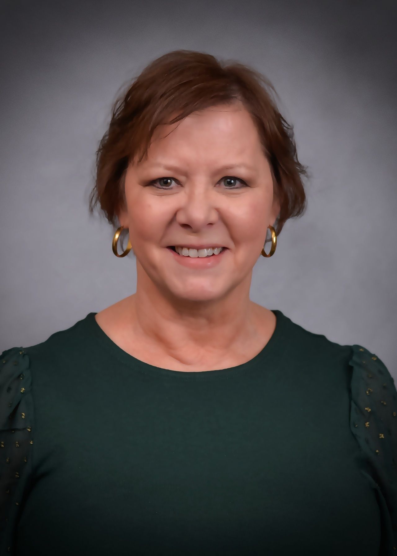 A woman wearing a green shirt and earrings is smiling for the camera.