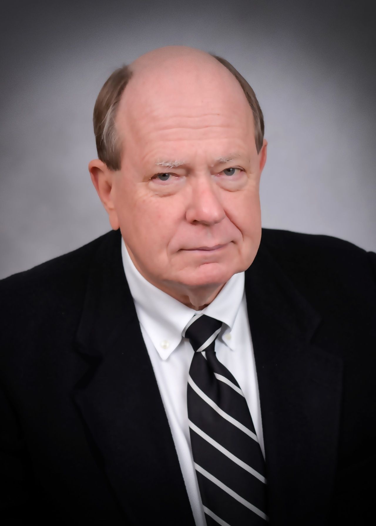A bald man in a suit and tie looks at the camera