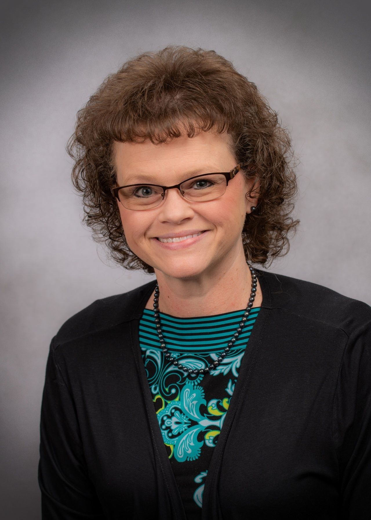 A woman wearing glasses and a blue shirt is smiling for the camera.