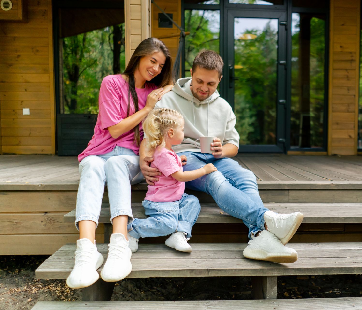 A family is sitting on the steps of a wooden house.
