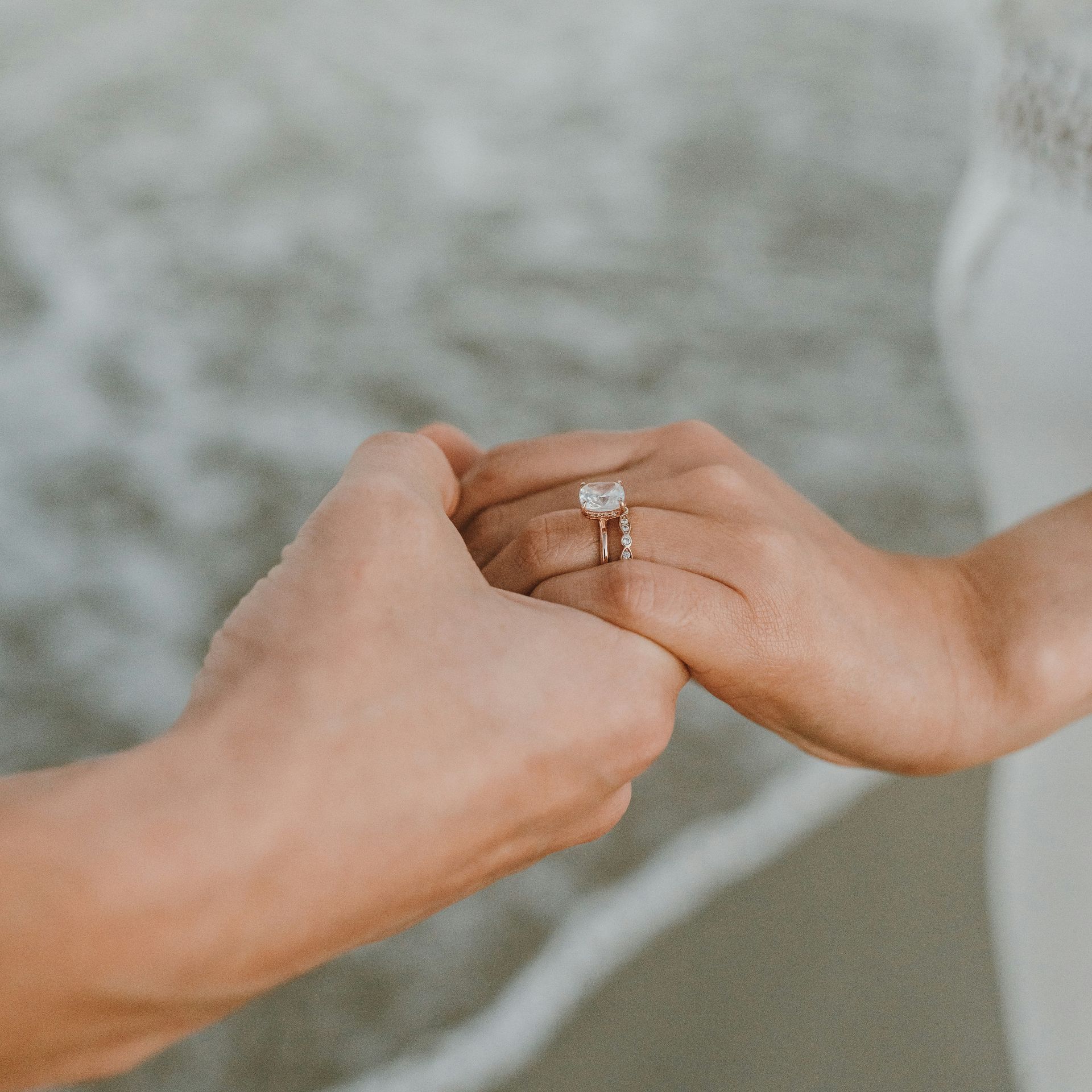A man is holding a woman 's hand with an engagement ring on her finger.