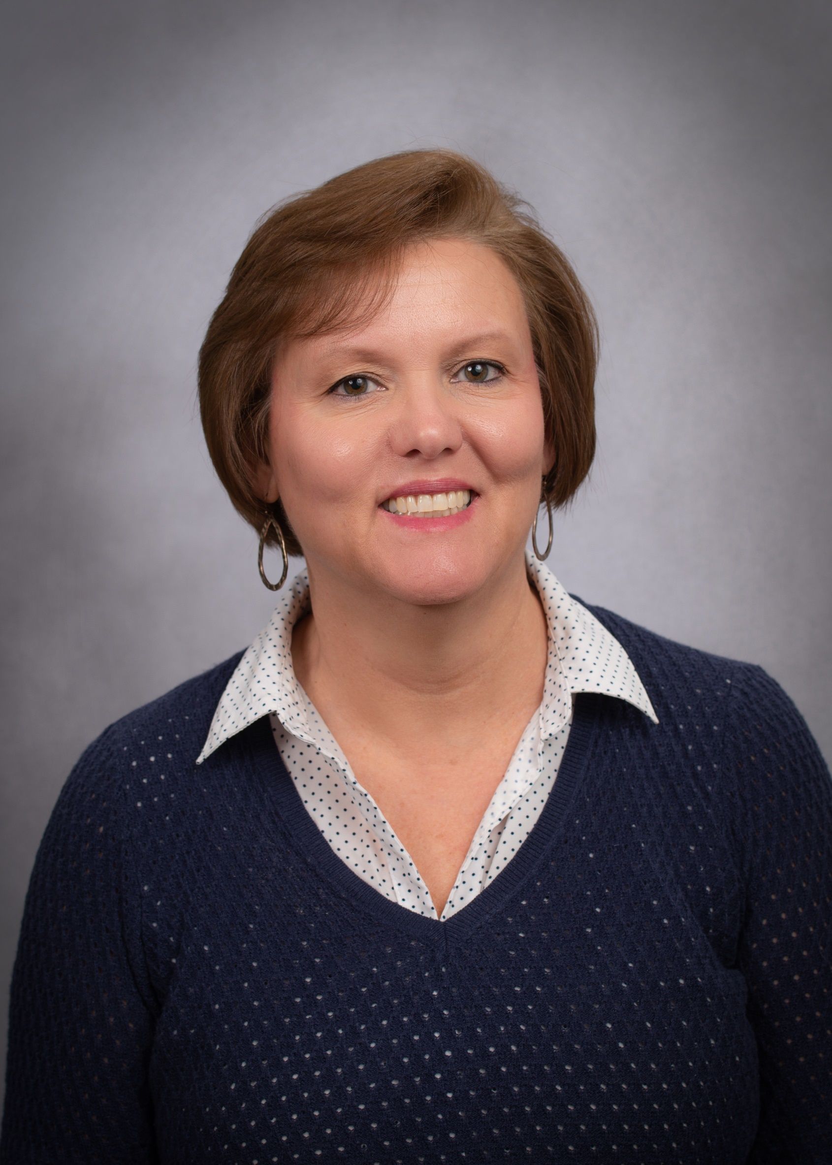 A woman in a blue sweater and white shirt is smiling for the camera.