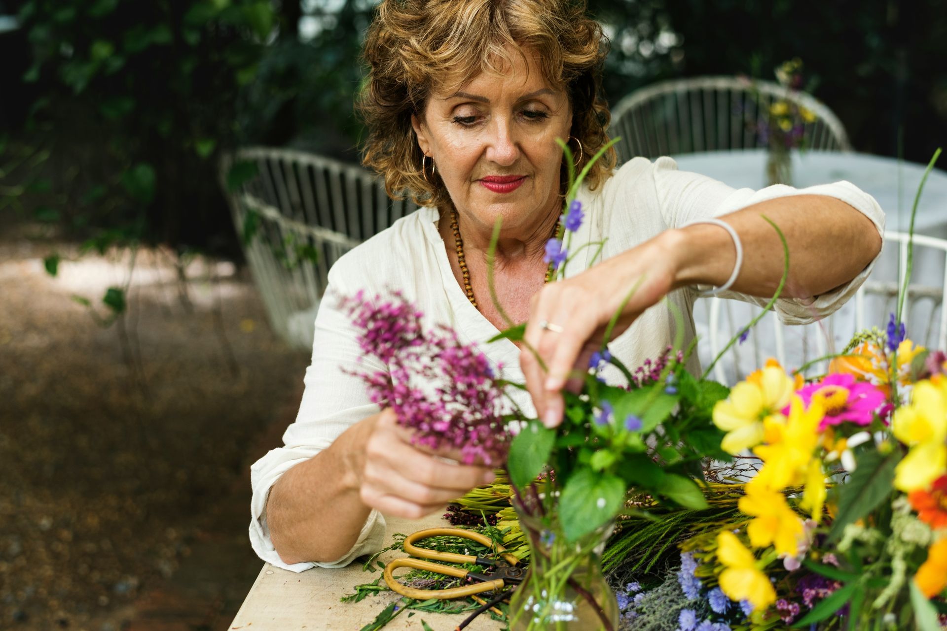 A woman is sitting at a table arranging flowers in a vase.