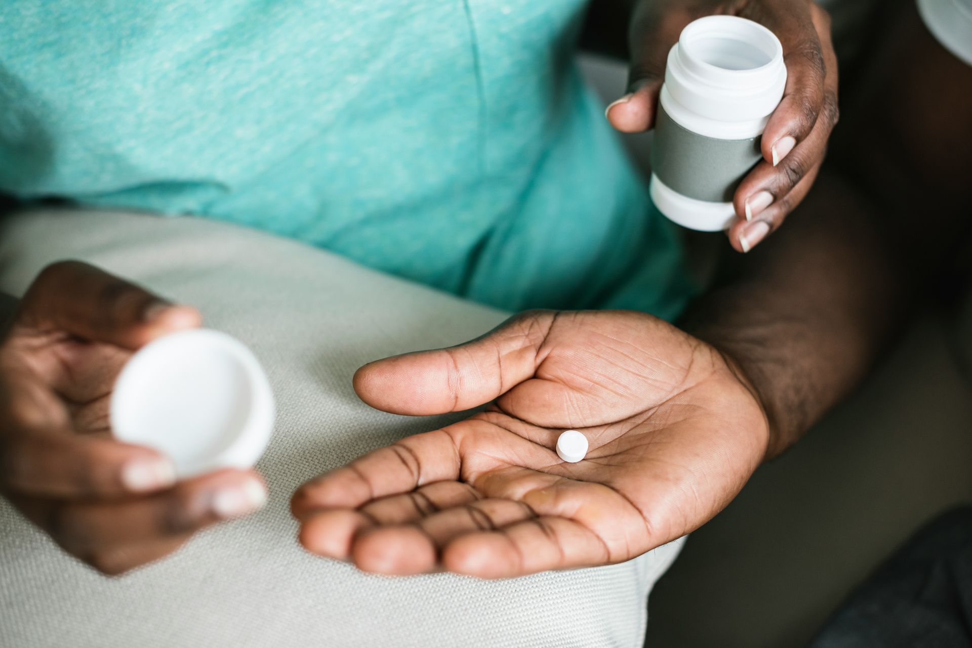 A person is holding a bottle of pills and a pill in their hand.