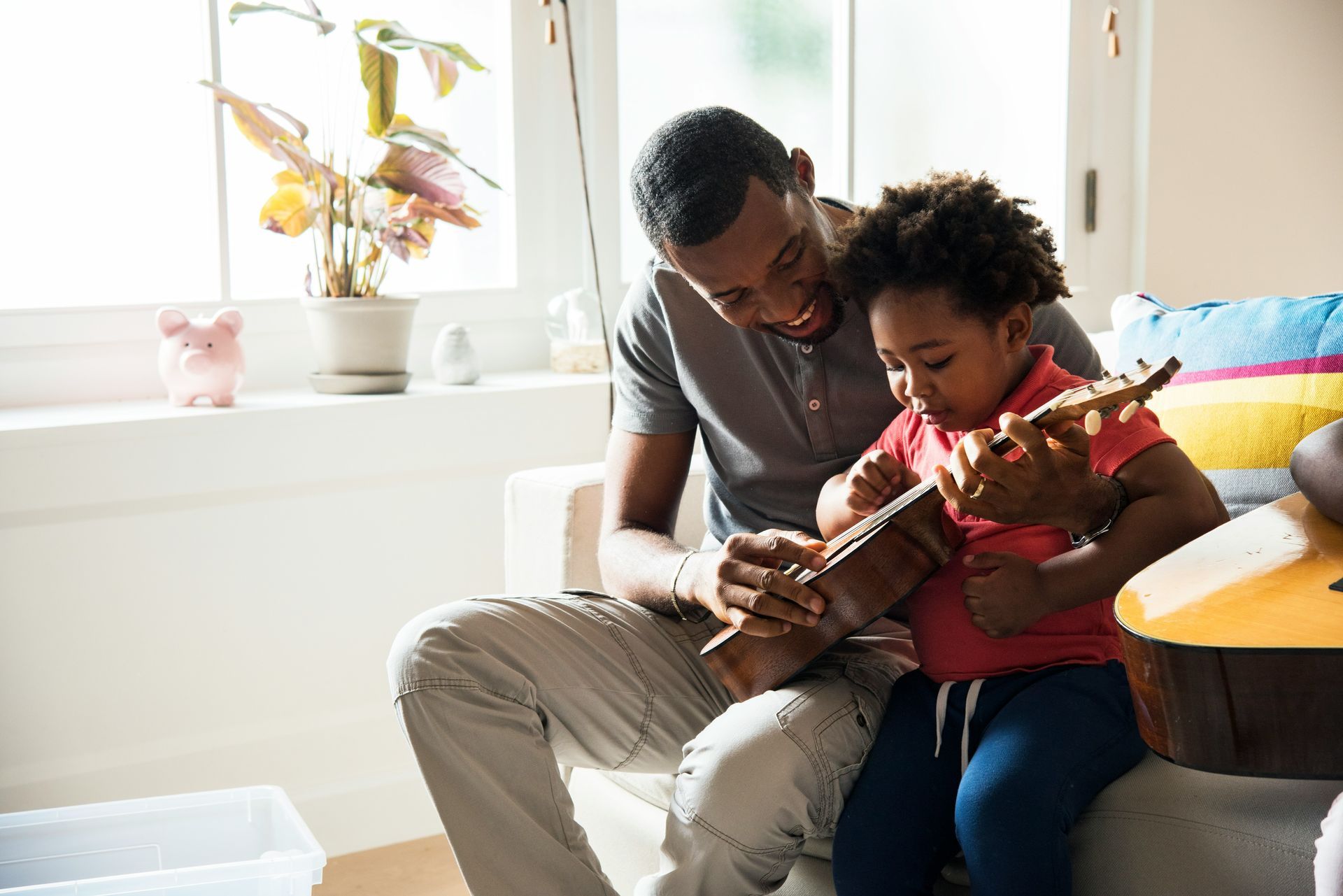 A man and a child are sitting on a couch playing a guitar.