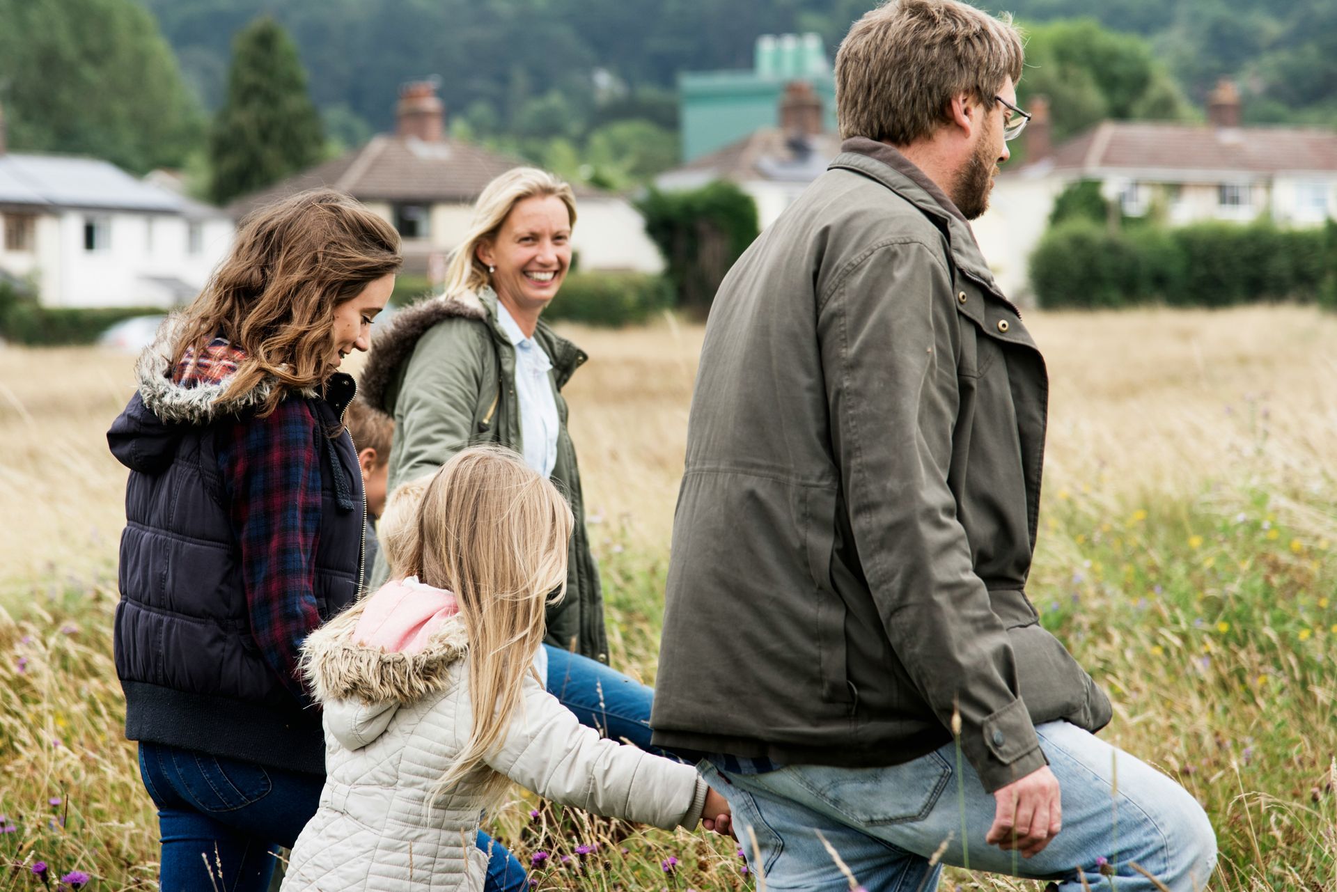 A family is walking through a field holding hands.