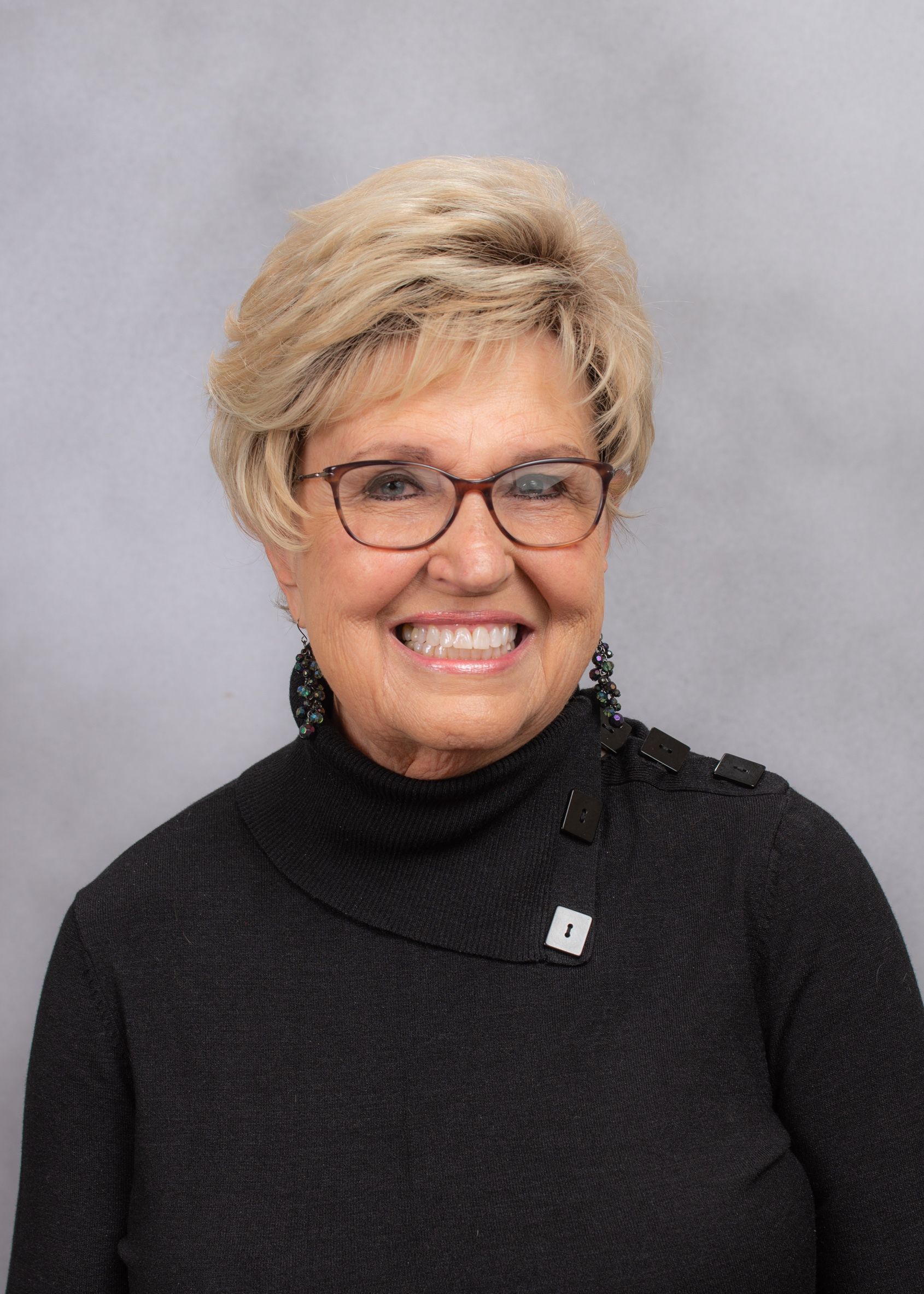 A woman wearing glasses and a black sweater is smiling for the camera.