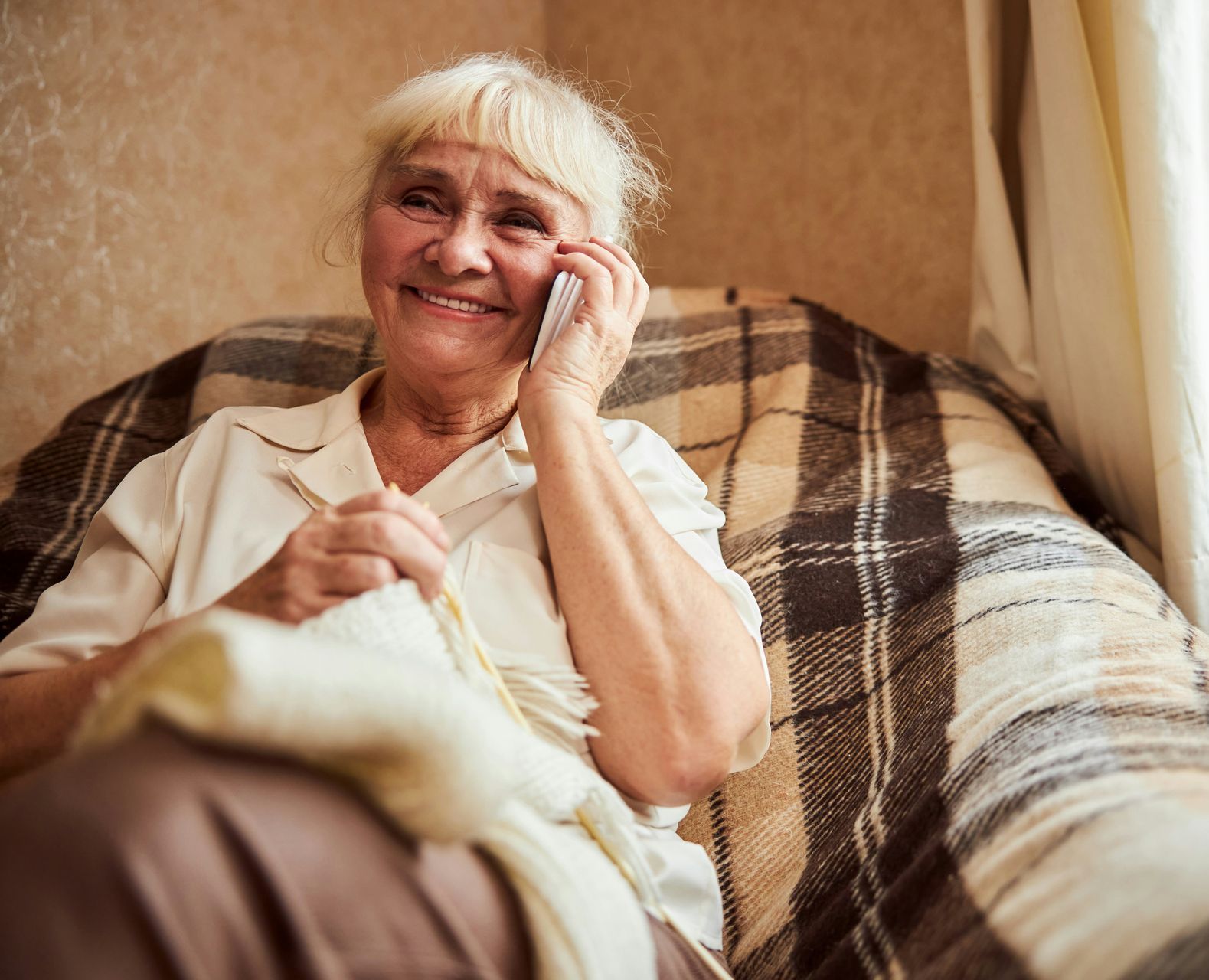 An elderly woman is sitting on a couch talking on a cell phone.