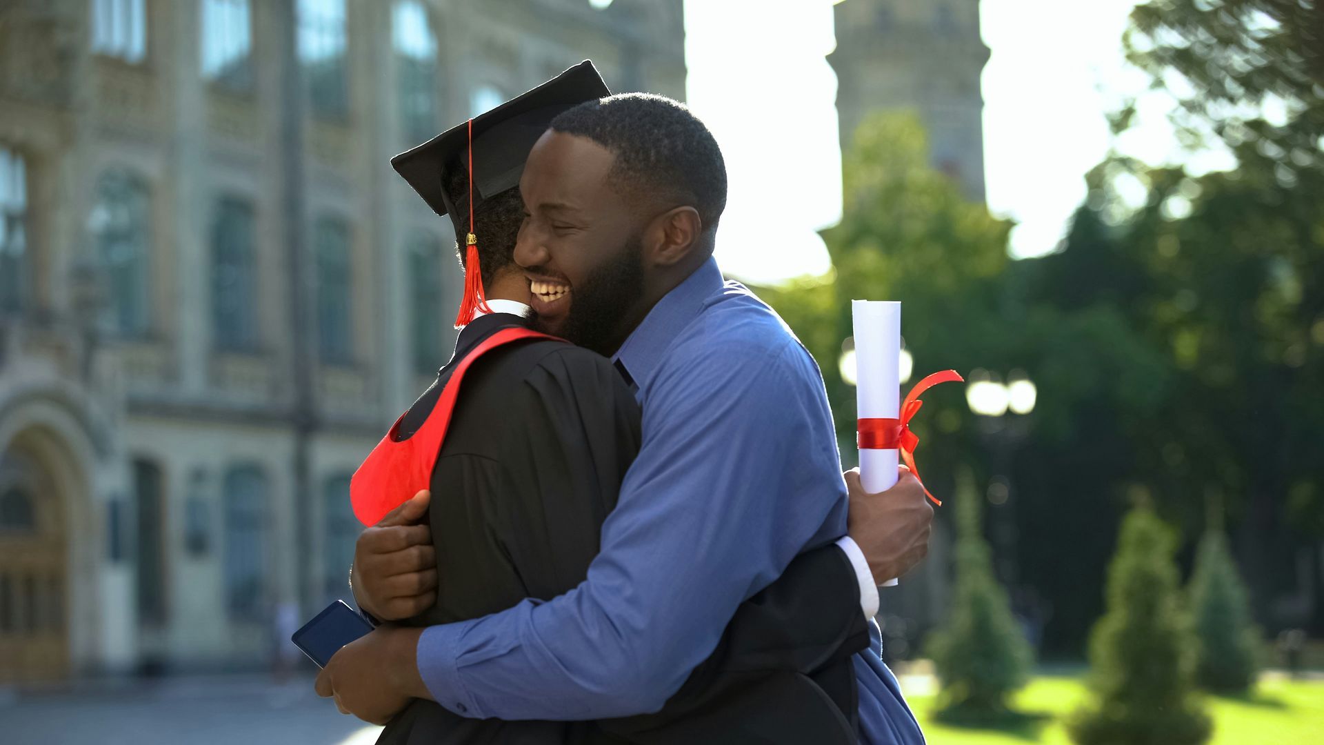 A man is hugging a woman in a graduation cap and gown.