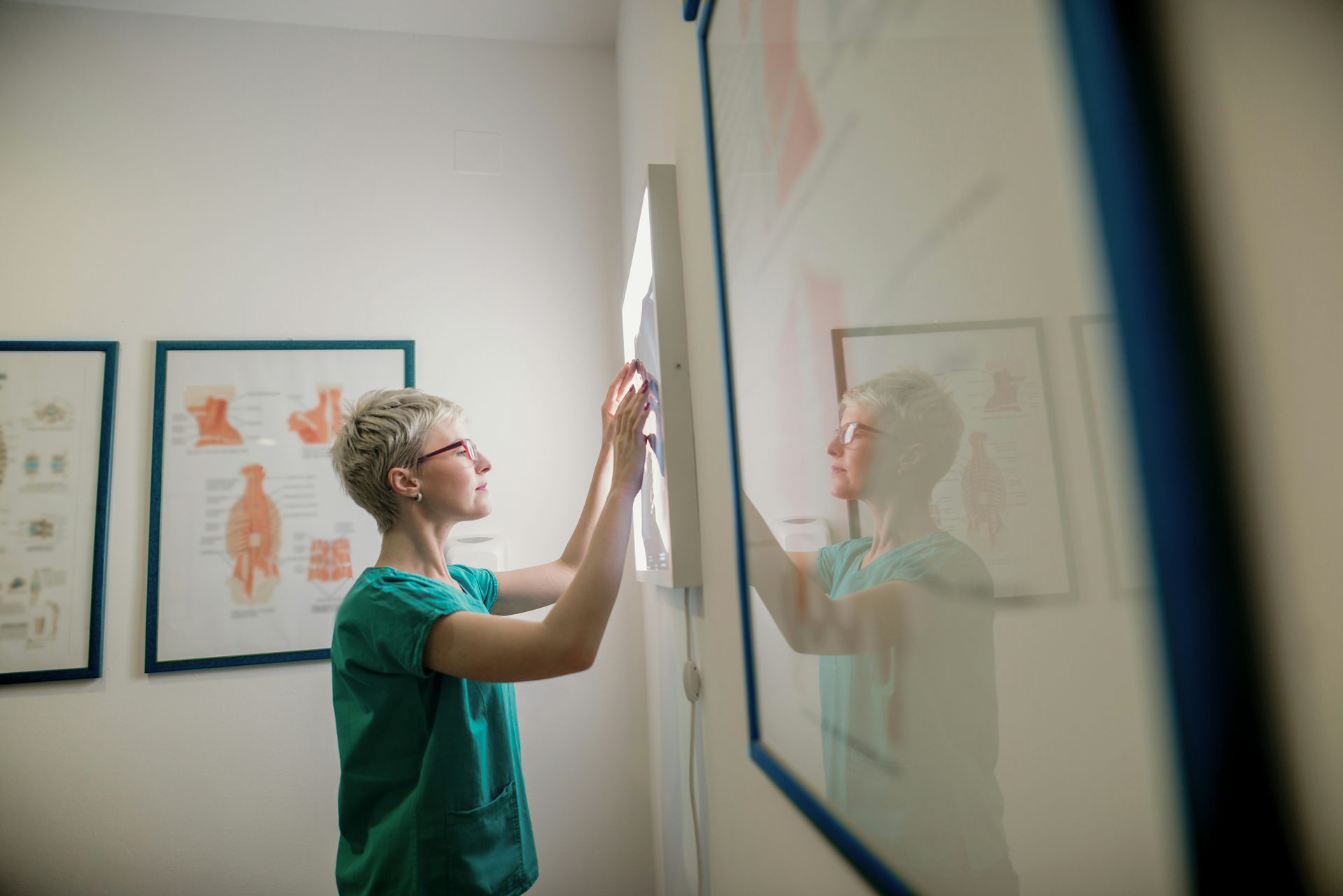 A woman is standing in a room looking at a picture on a wall.