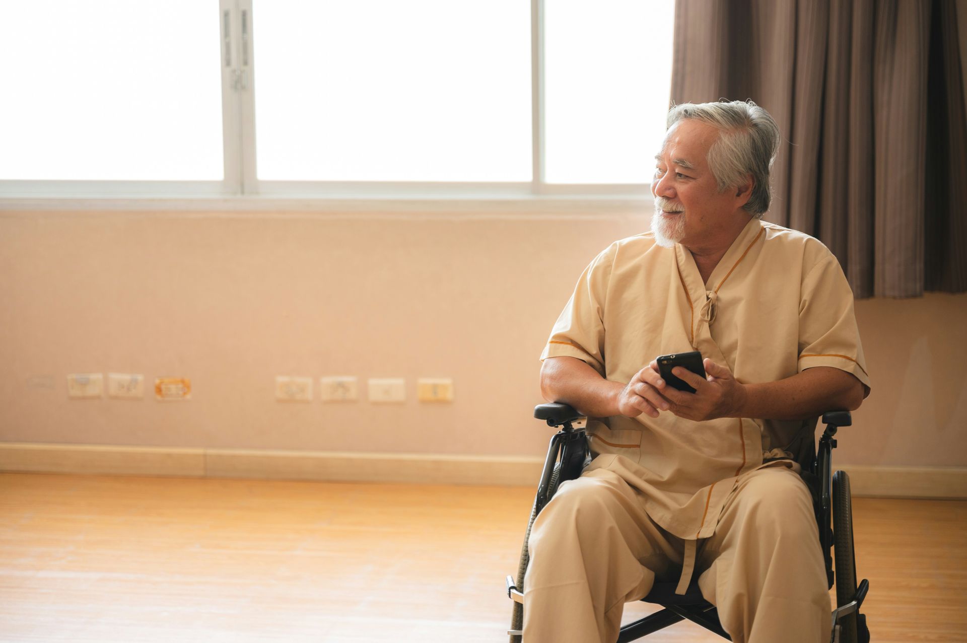 An elderly man is sitting in a wheelchair using a cell phone.