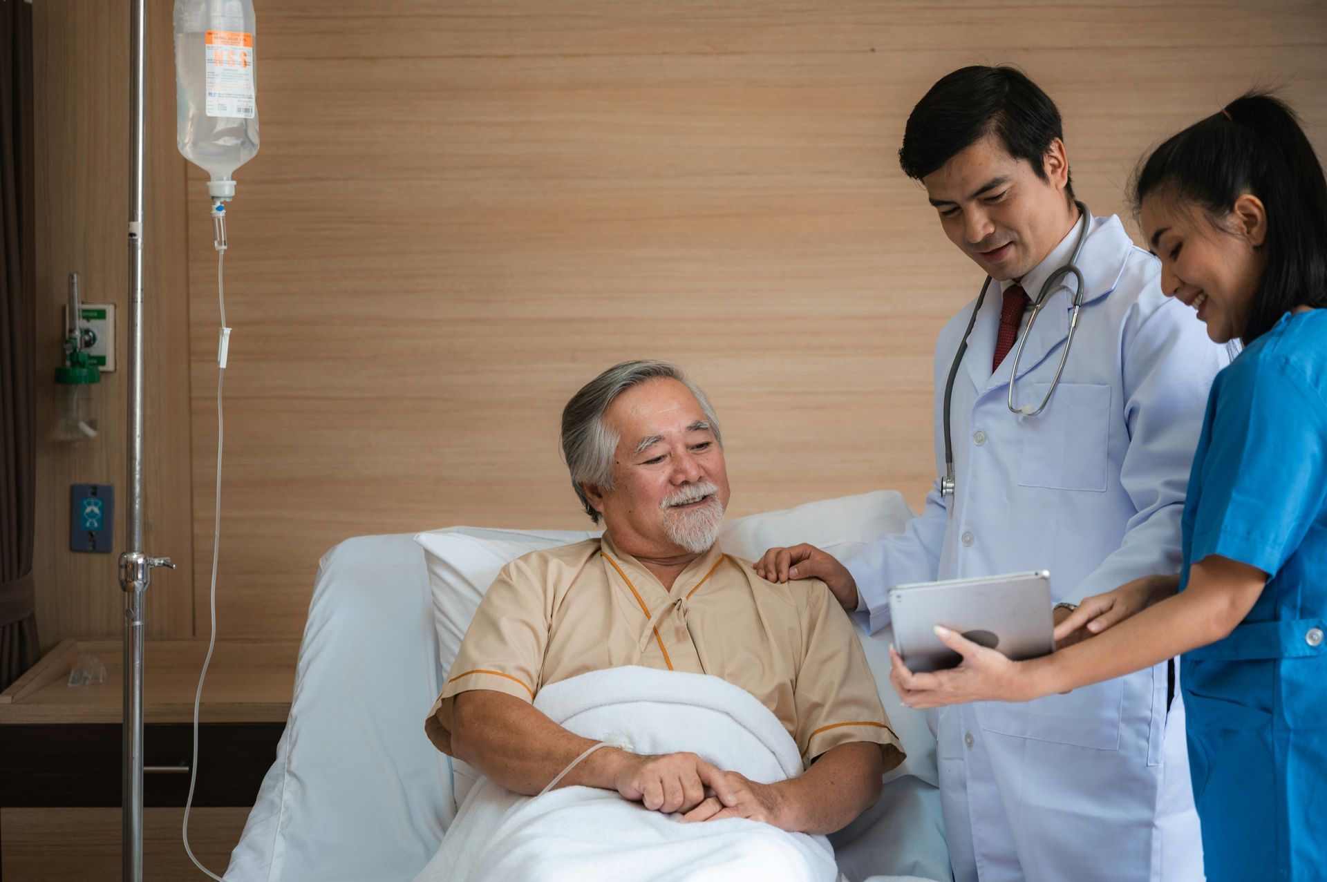 A doctor and nurse are talking to an elderly man in a hospital bed.