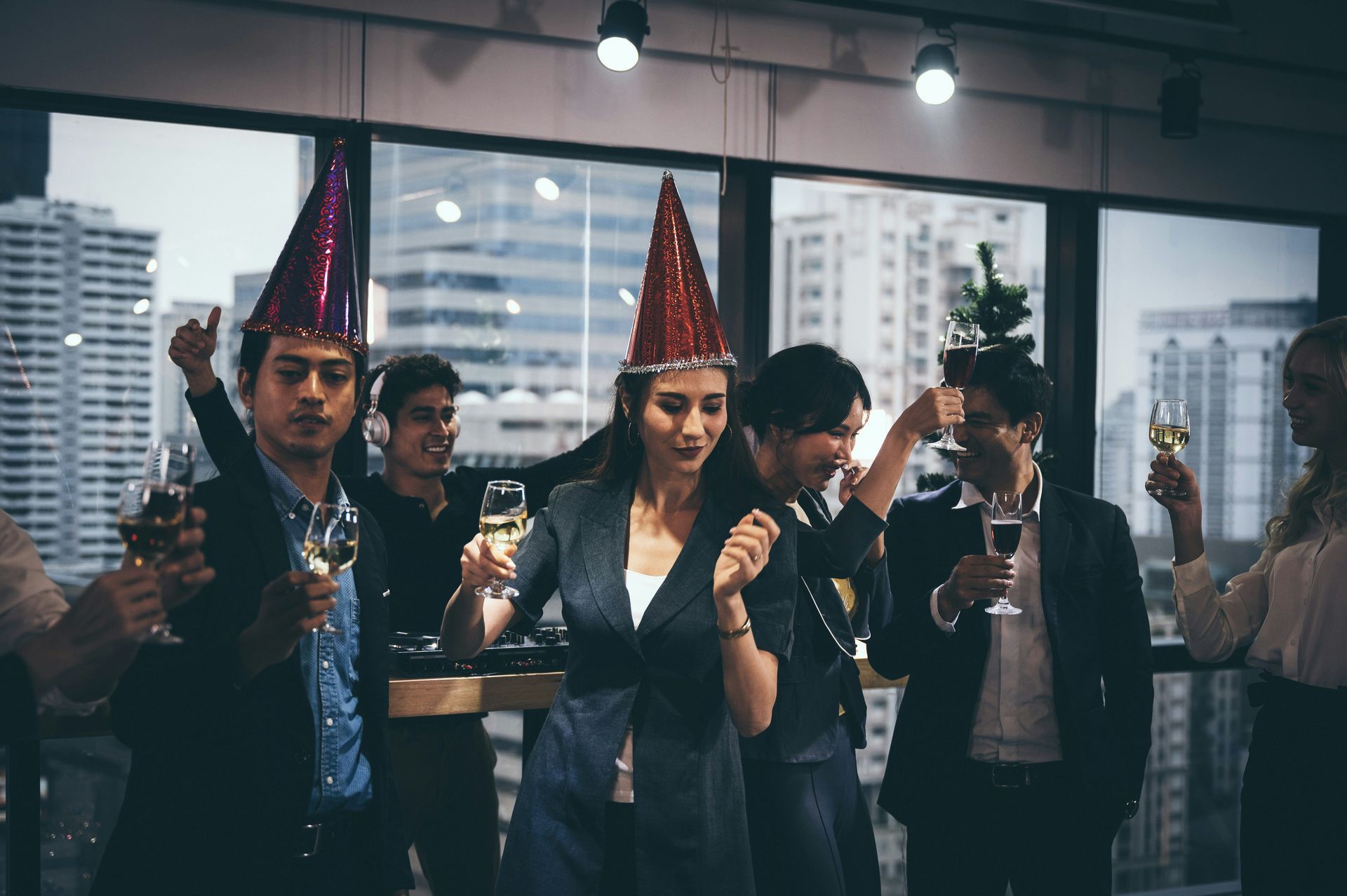 A group of people wearing party hats and holding champagne glasses are dancing at a new year 's eve party.
