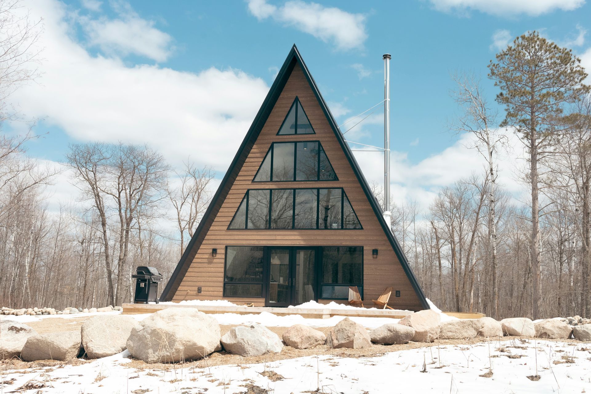 A triangle shaped house in the middle of a snowy forest.