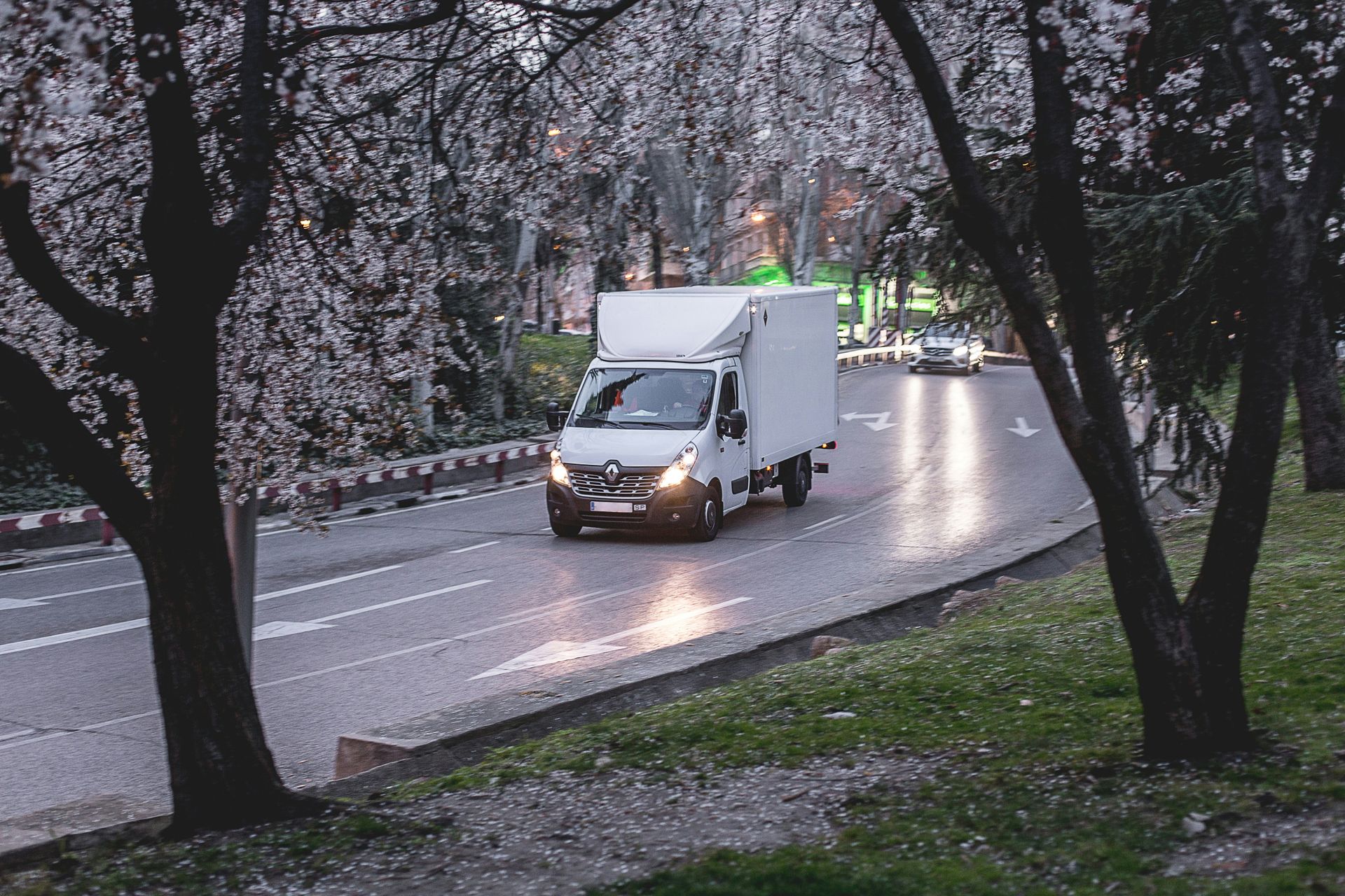 A white van is driving down a road surrounded by trees.