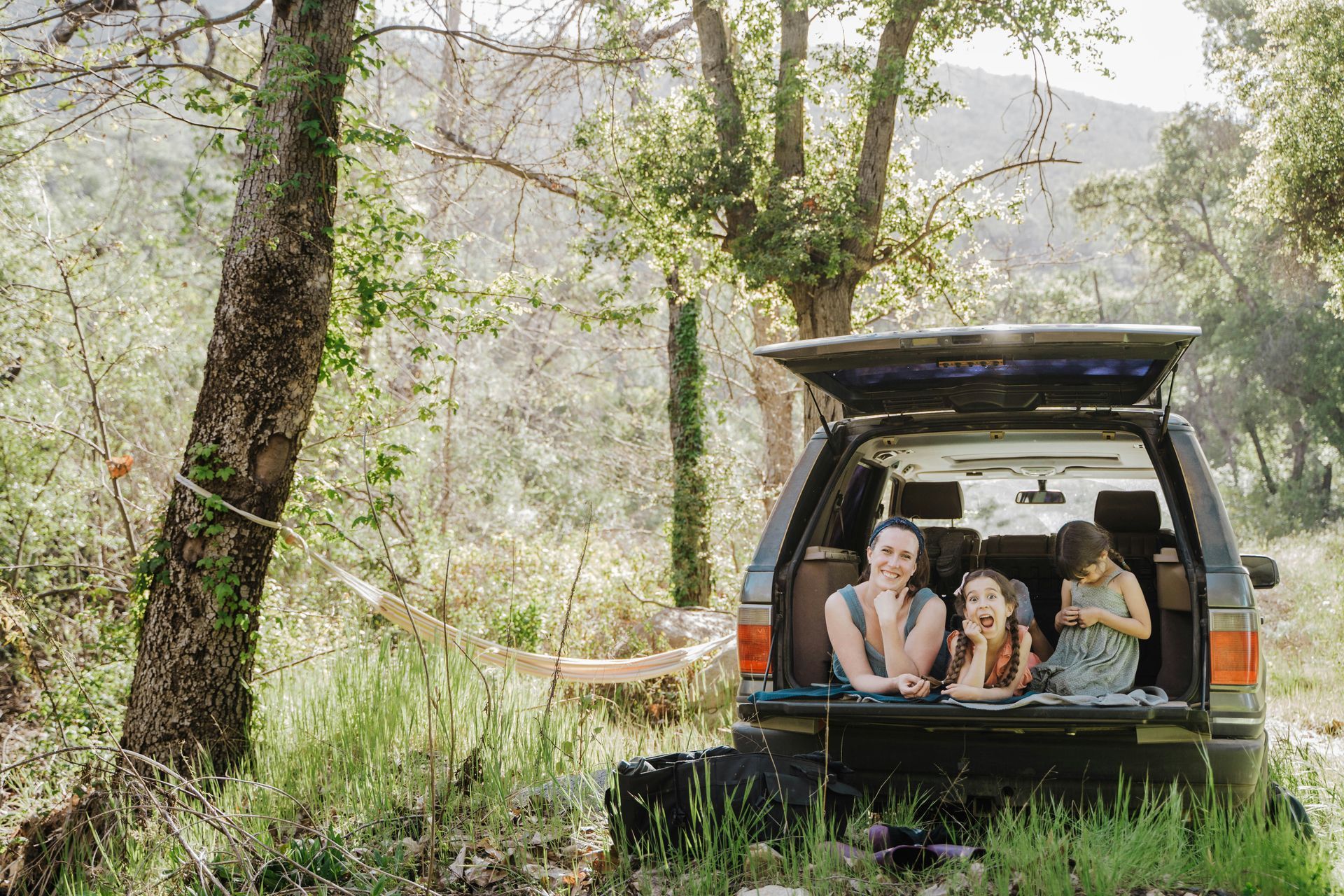 A family is sitting in the back of a car in the woods.