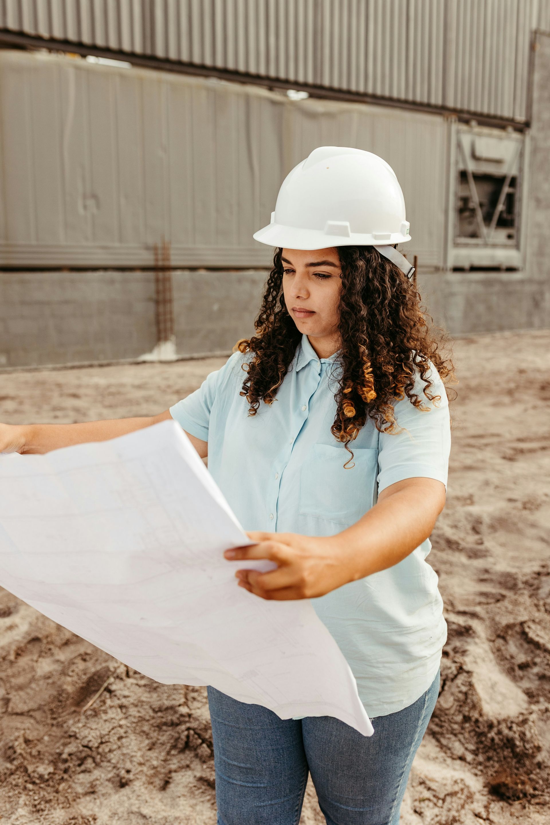 A woman wearing a hard hat is looking at a blueprint on a construction site.