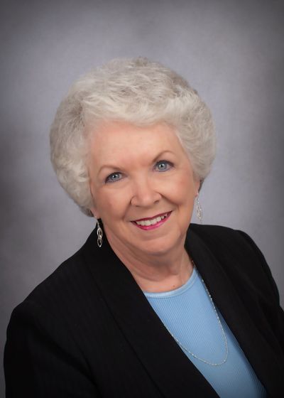 A woman wearing a black jacket and a blue shirt is smiling for the camera.