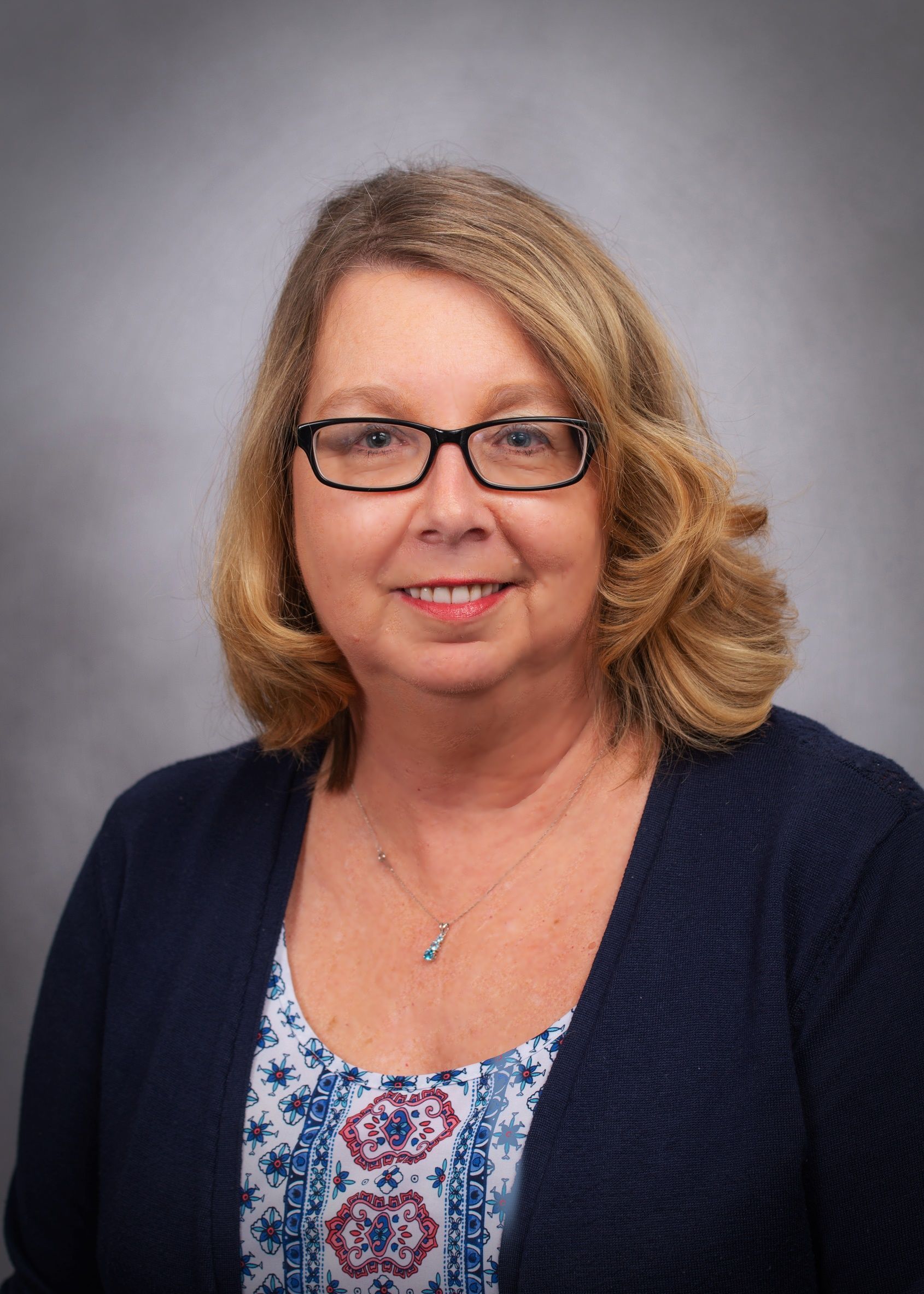 A woman wearing glasses and a blue sweater is smiling for the camera.