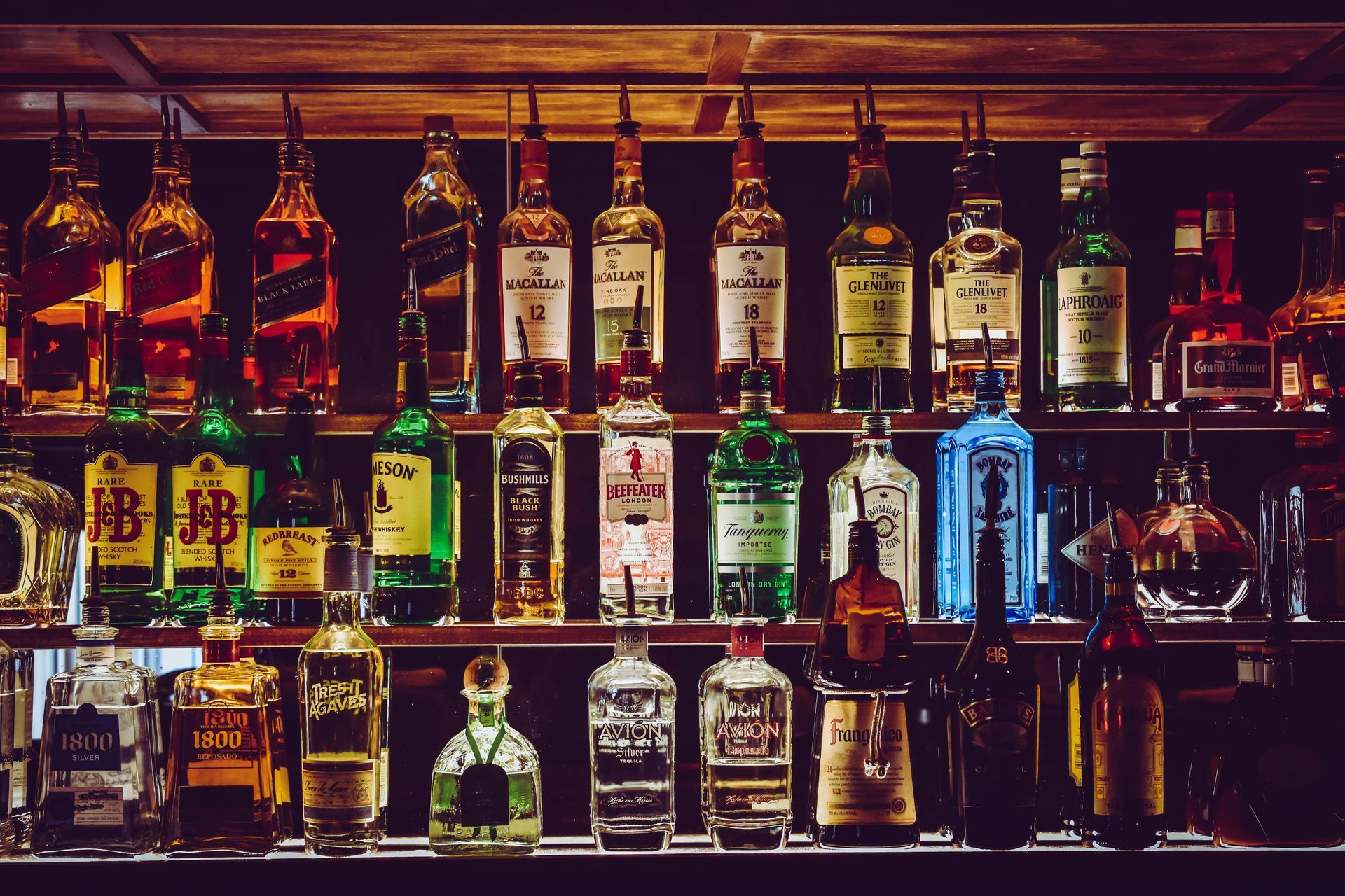 A row of bottles of liquor are lined up on a bar shelf.