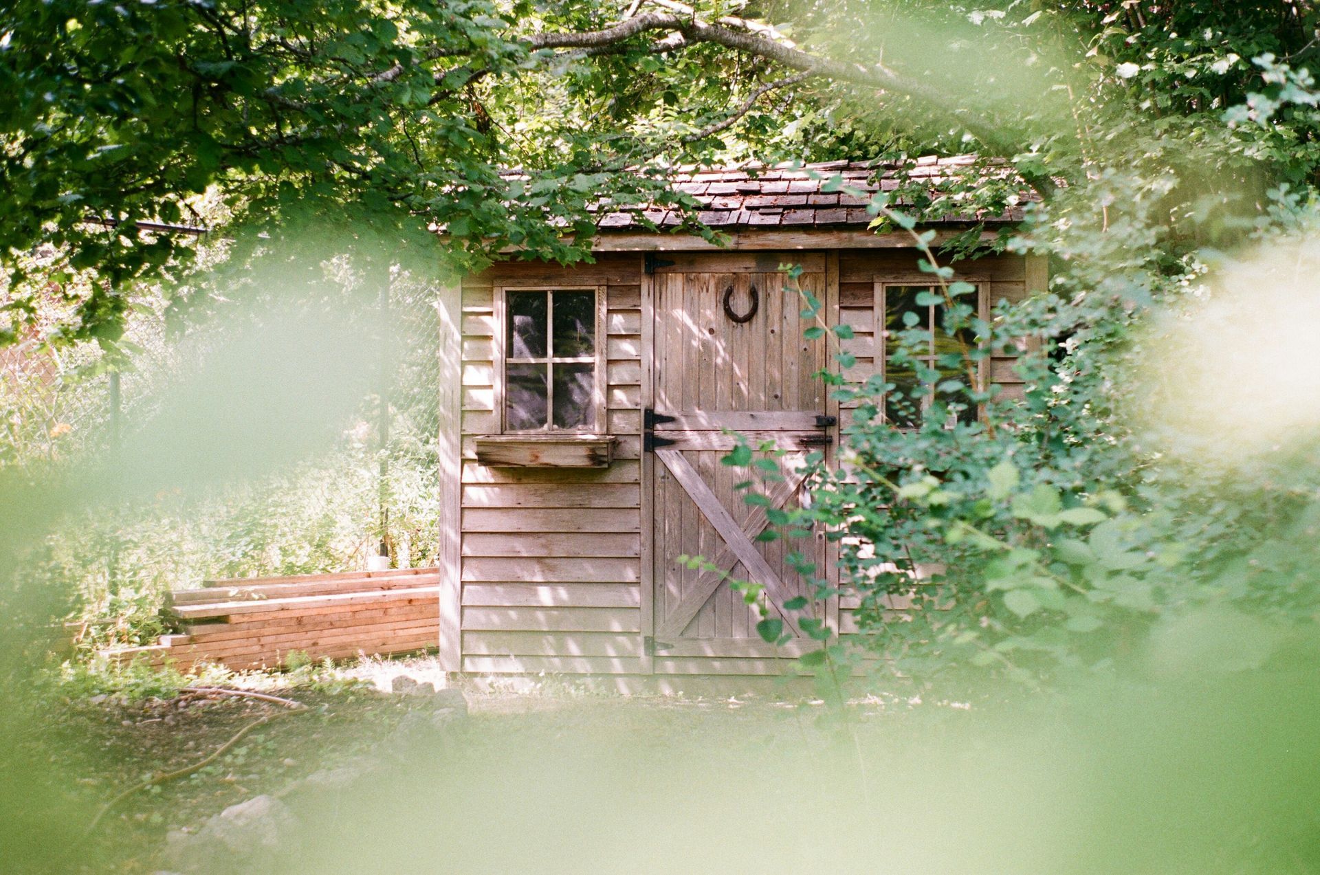 A small wooden shed with a horseshoe on the door is surrounded by trees.
