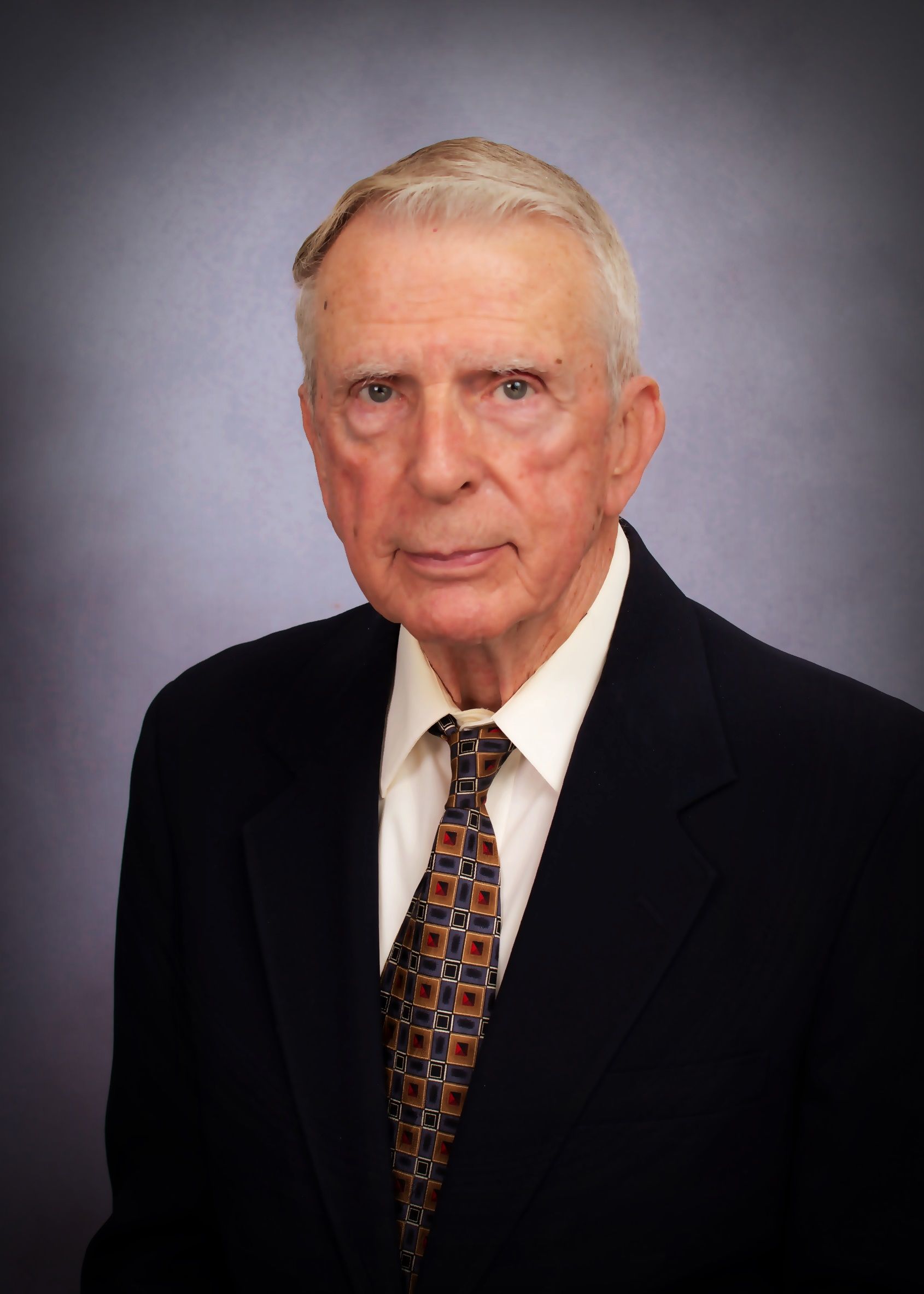 A man in a suit and tie stands in front of a blue background