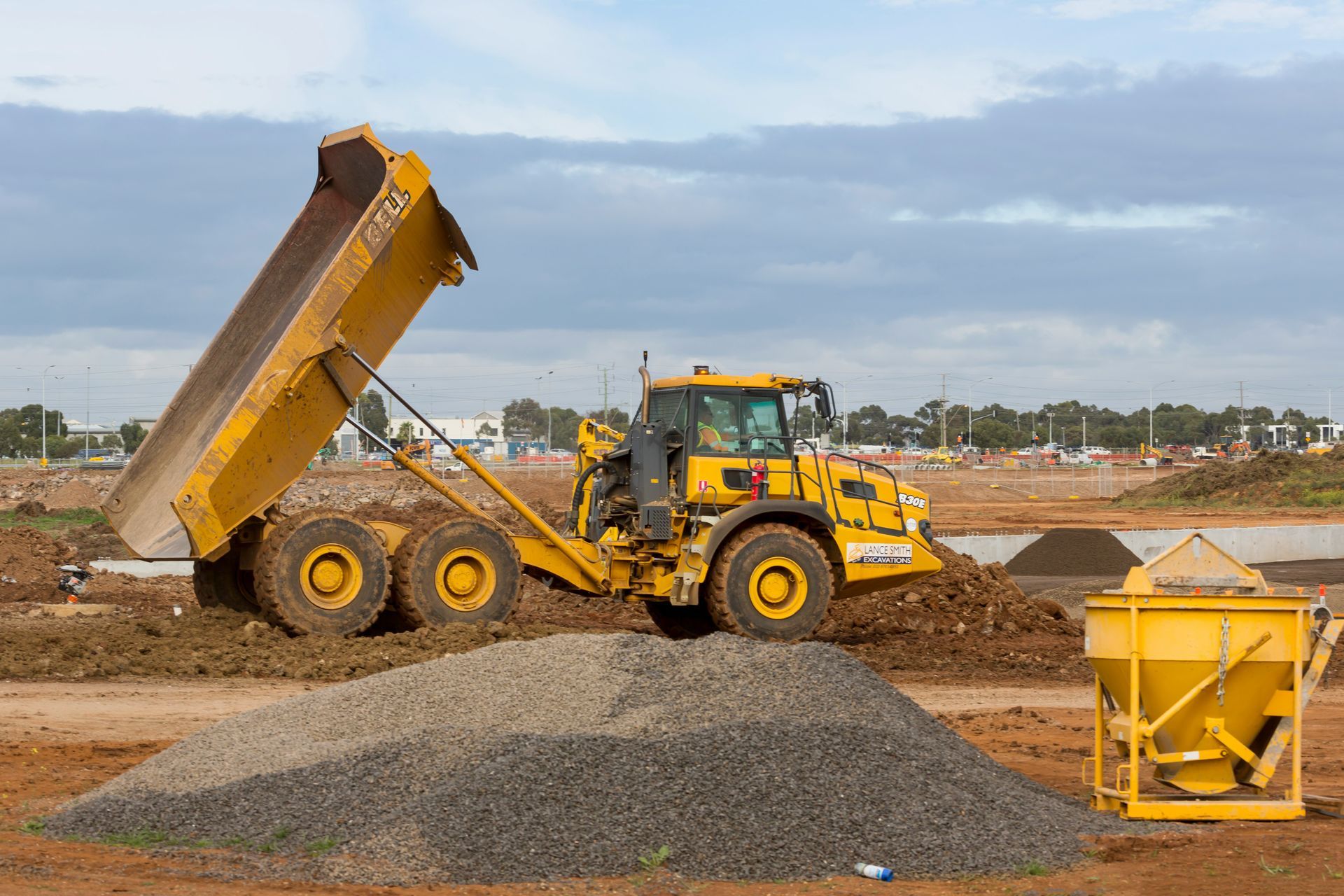 A yellow dump truck is loading gravel on a construction site.