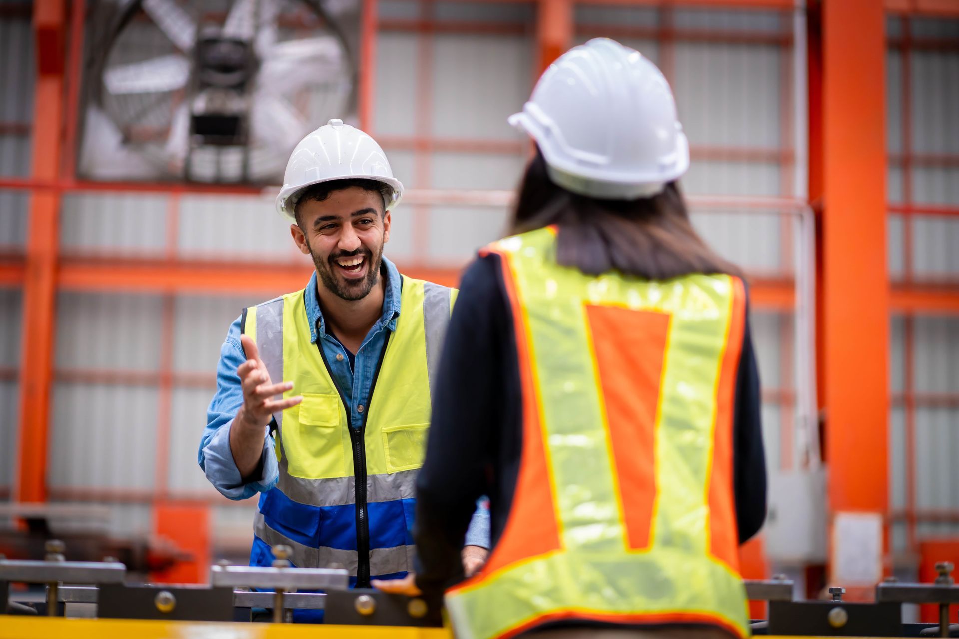 A man and a woman are talking to each other in a factory.