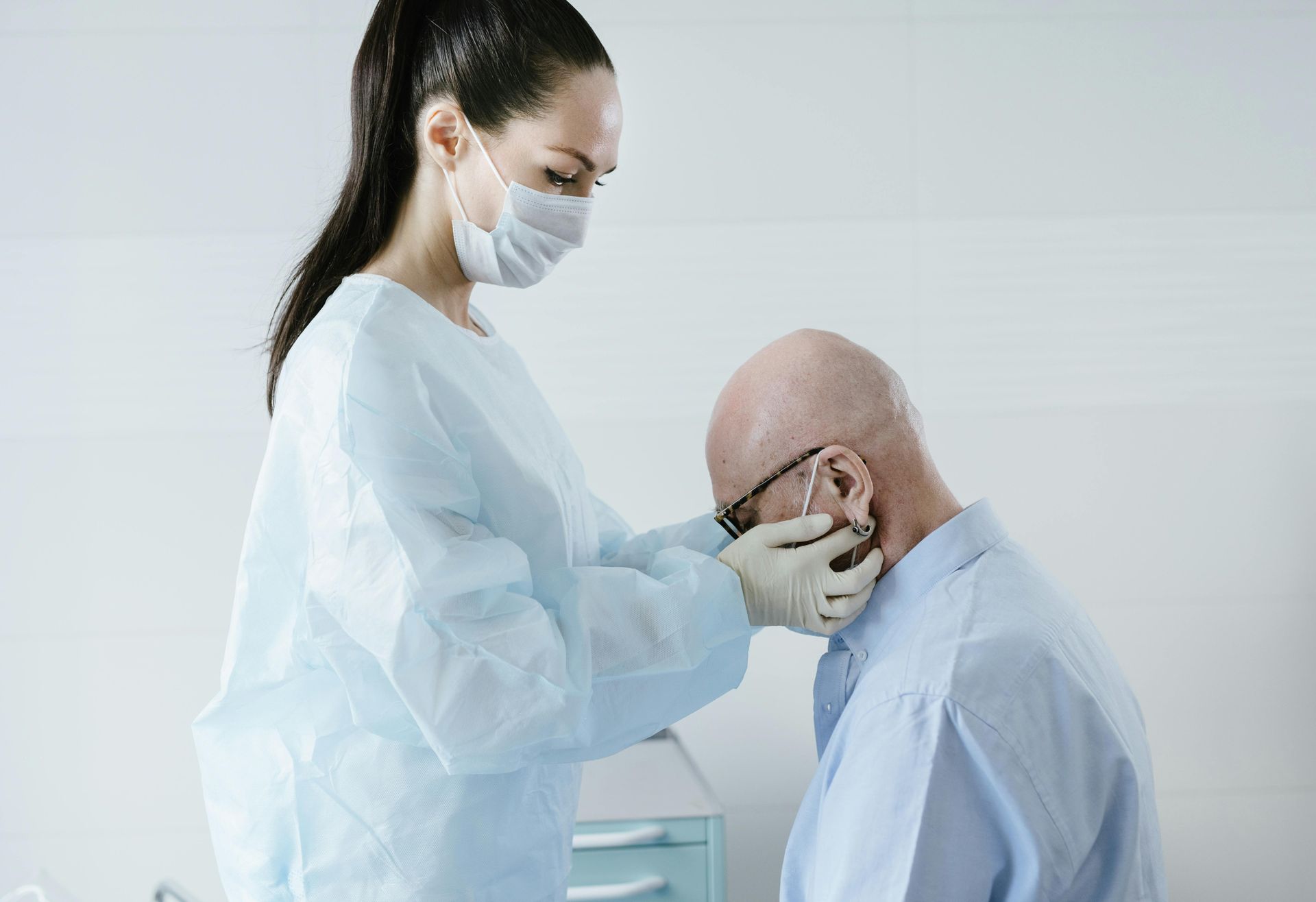 A doctor with a mask on is examining a patients' lymph nodes on their neck