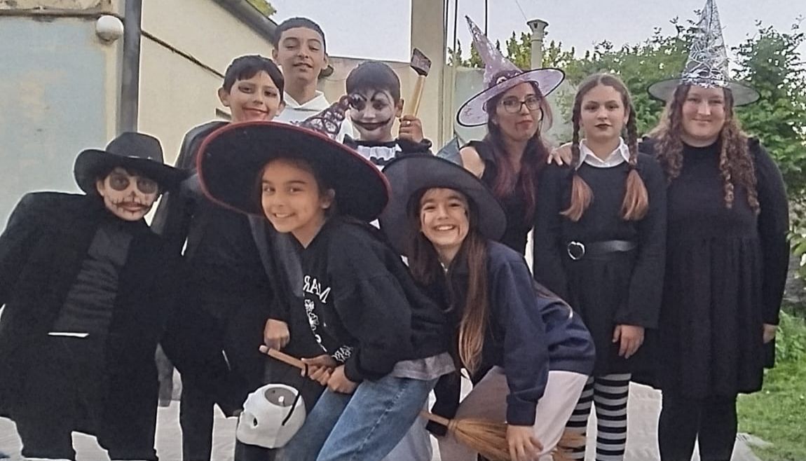 Un grupo de personas vestidas con disfraces, sombreros y maquillaje negros de Halloween, posando juntas al aire libre.
