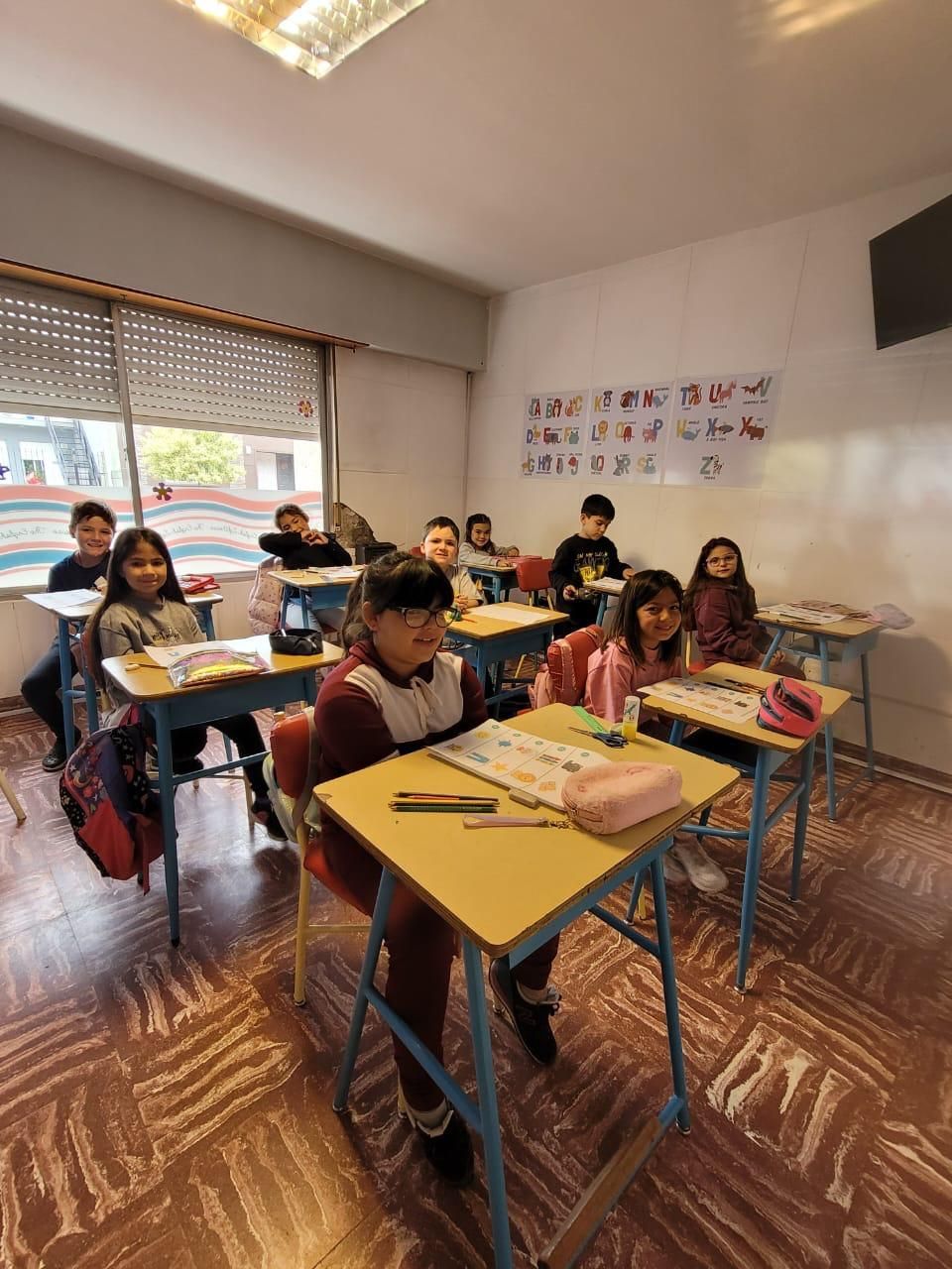 Un grupo de estudiantes sentados en pupitres individuales en un aula, mirando hacia la cámara.