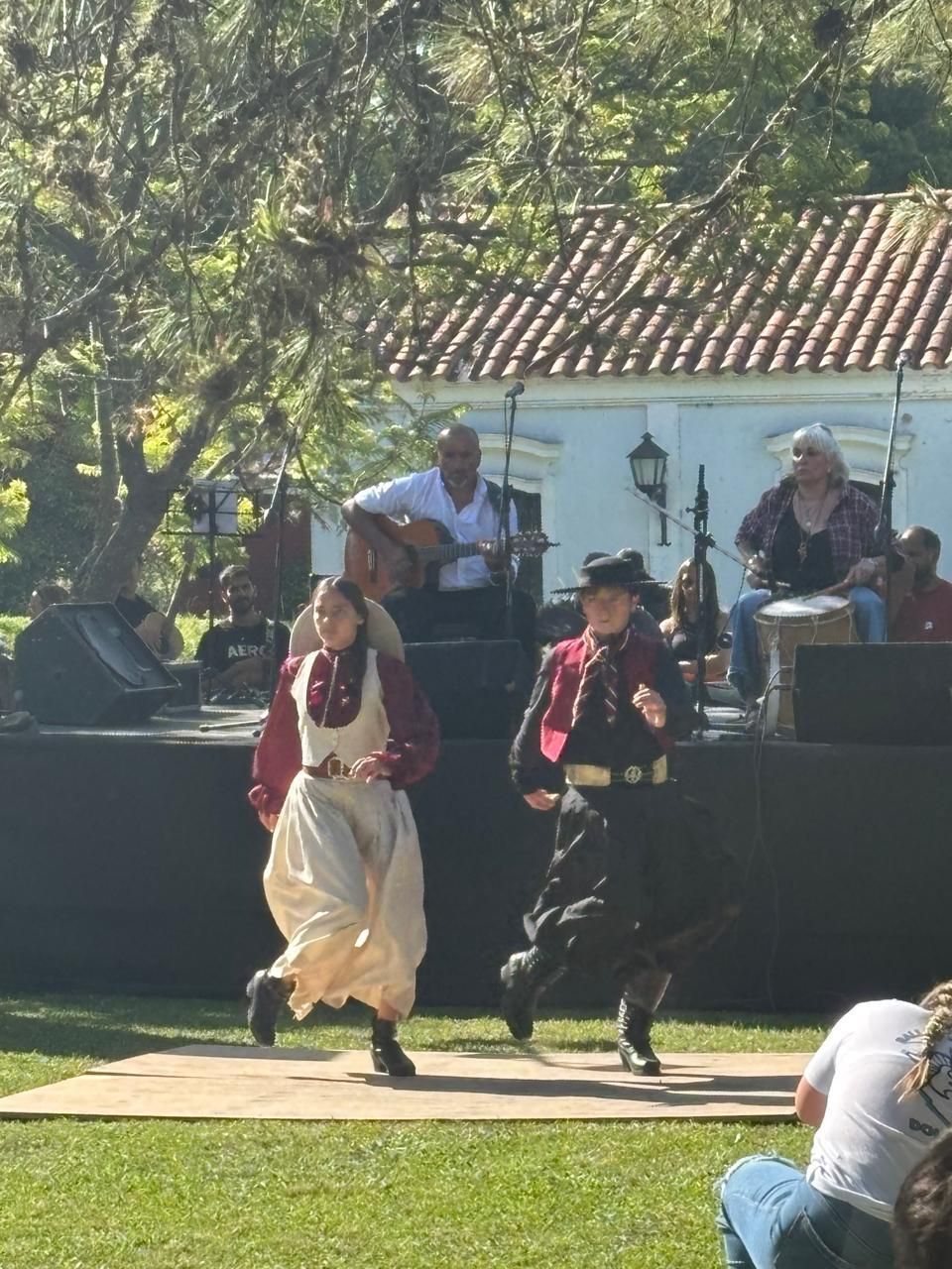 Una persona baila flamenco vestida de rojo y blanco mientras otras personas permanecen cerca o tocan la guitarra en un patio.