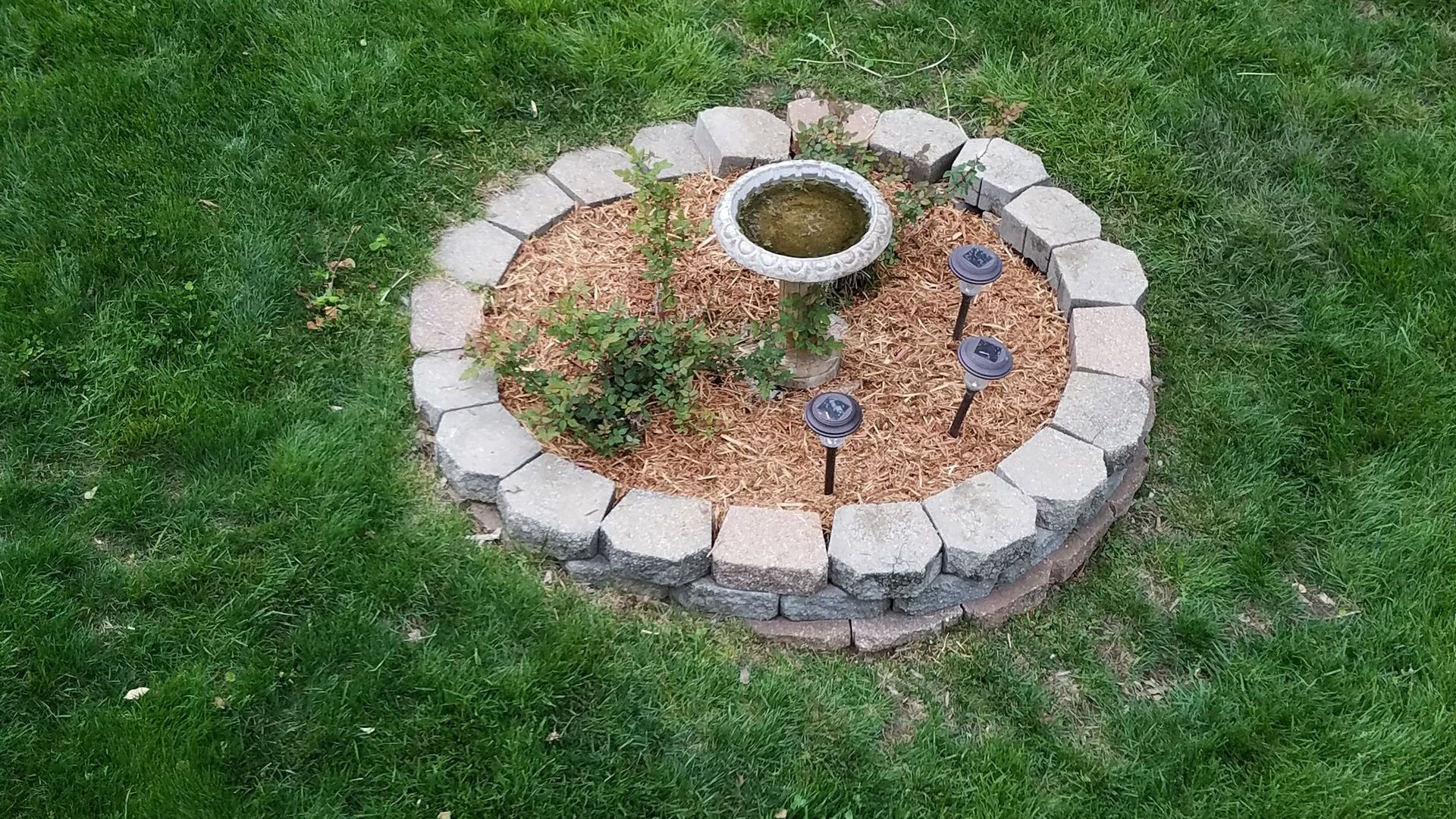 A bird bath is sitting in the middle of a circled hardscaping and softscaping