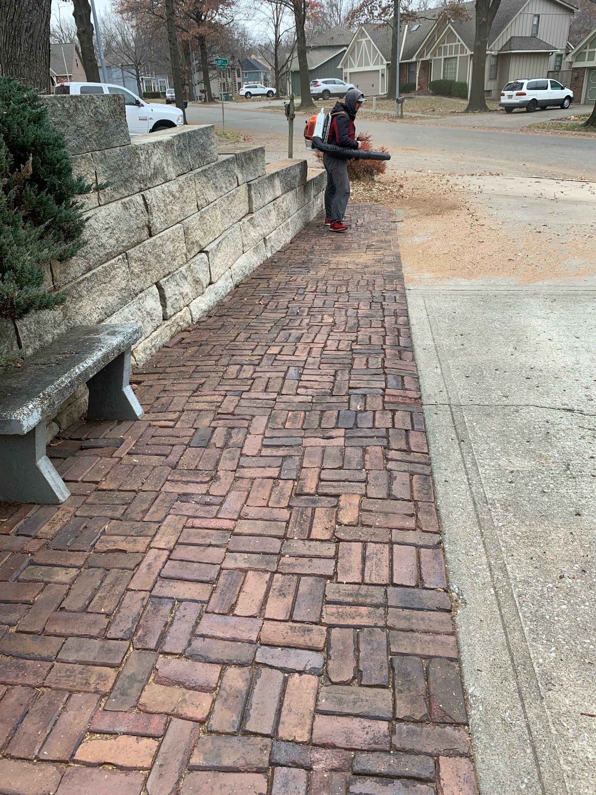 A person is standing on a brick sidewalk next to a bench.