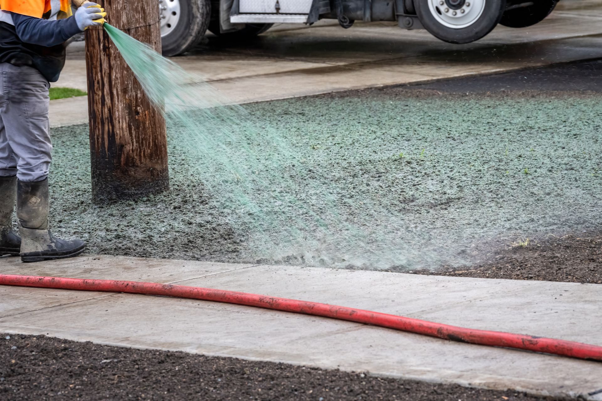 A man is spraying green slurry of seed and fertilizer on a bare yard for hydroseeding