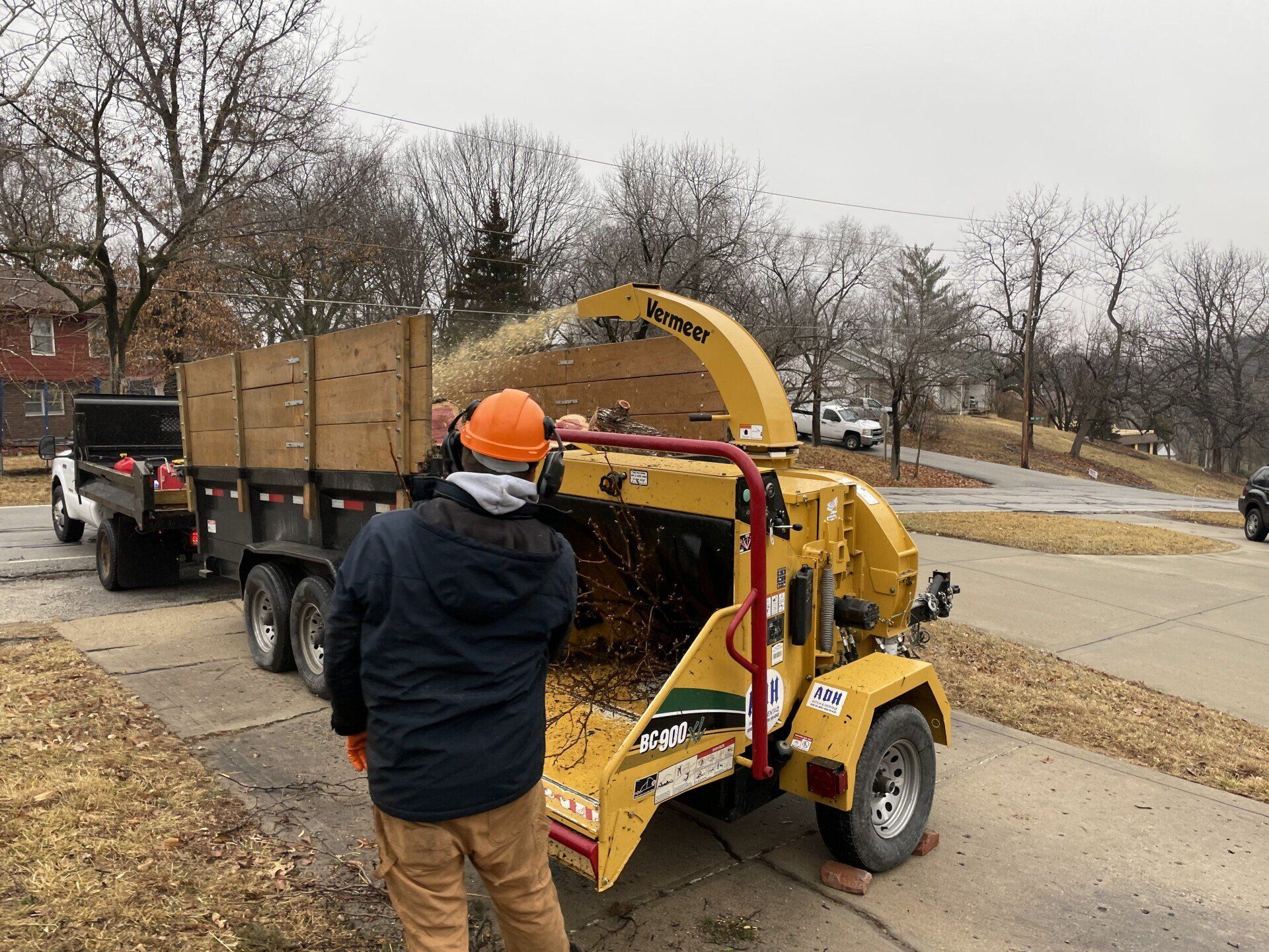 A man is standing next to a tree chipper on the side of the road.