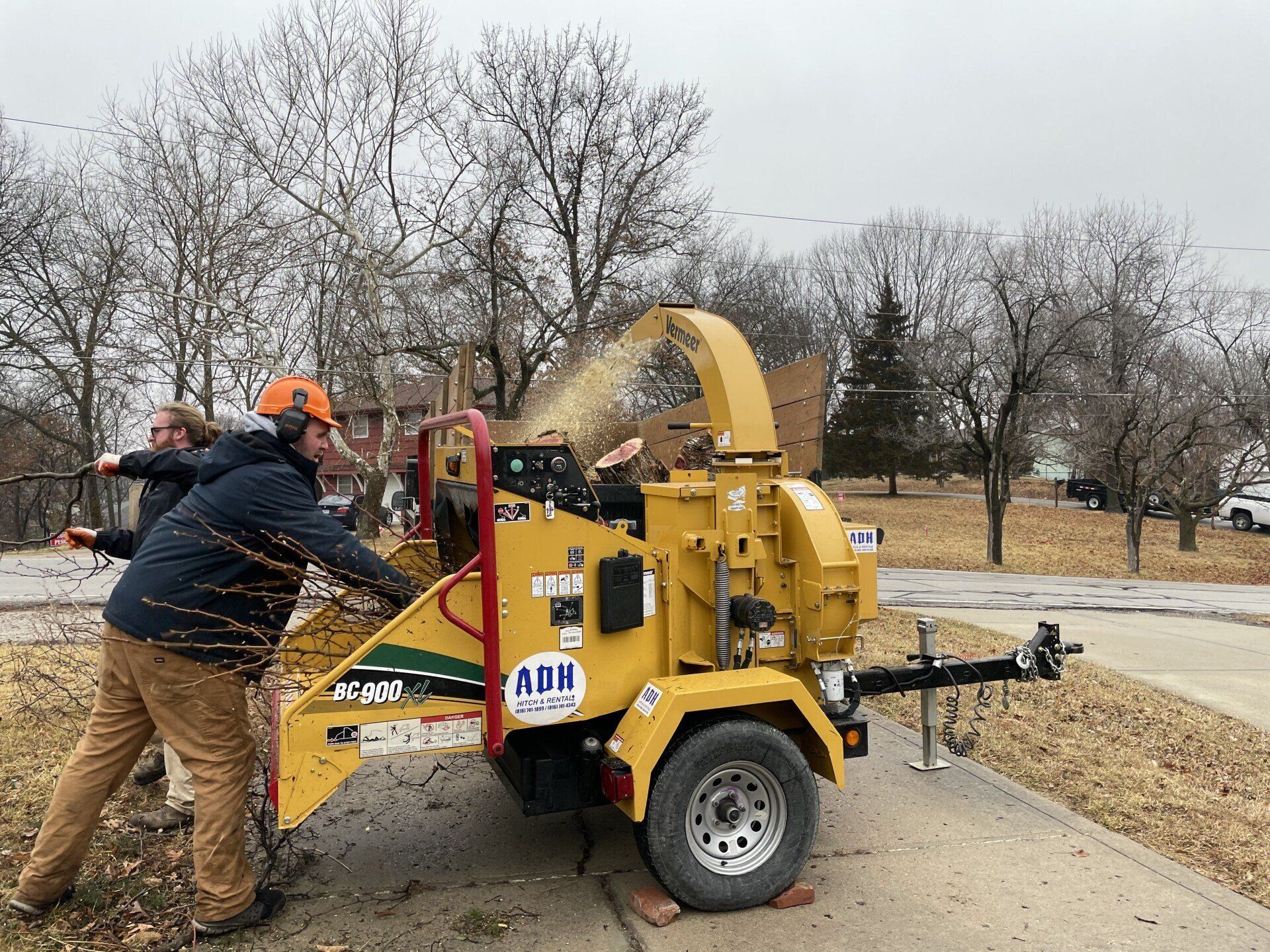 A man is pushing a tree chipper down a sidewalk.
