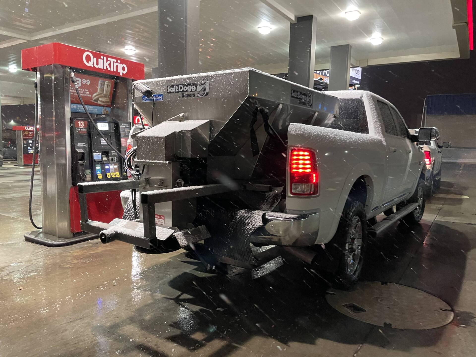 A white truck is parked at a gas station in the snow.