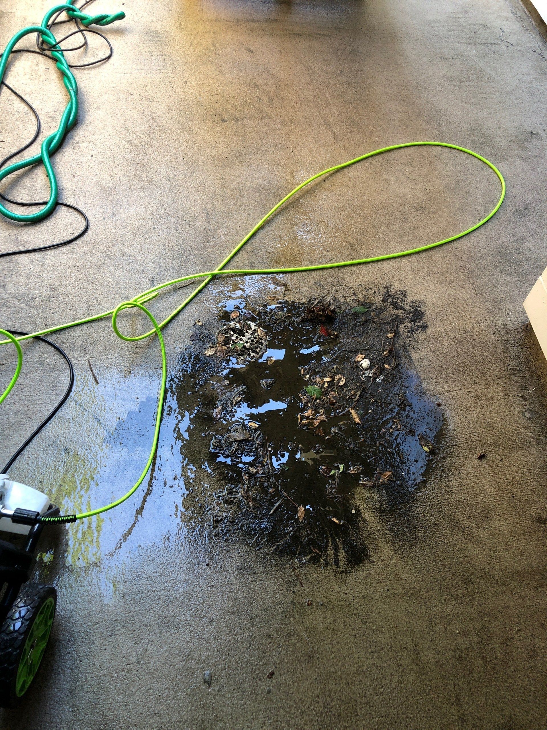 A green hose is laying on a dirty concrete floor.